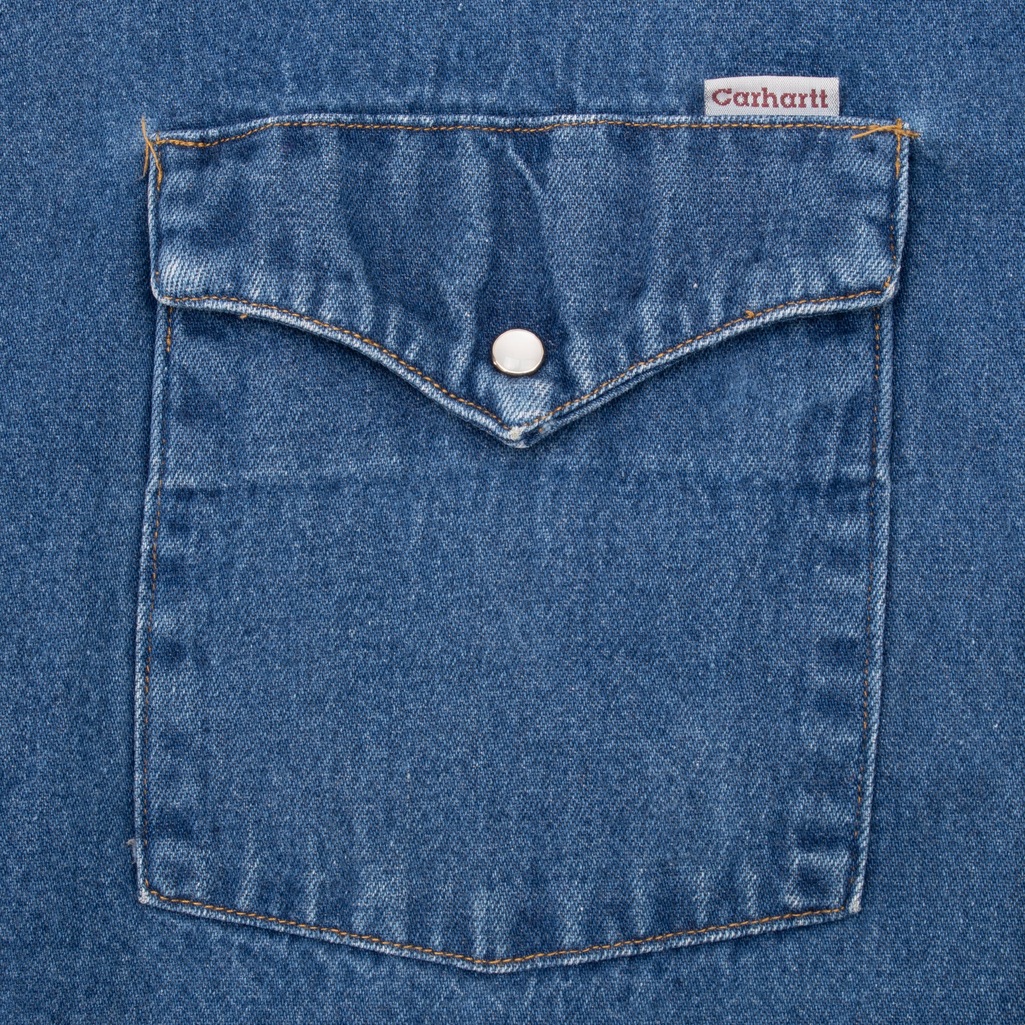 Close-up of blue denim chest pocket with pearl snap and Carhartt tab