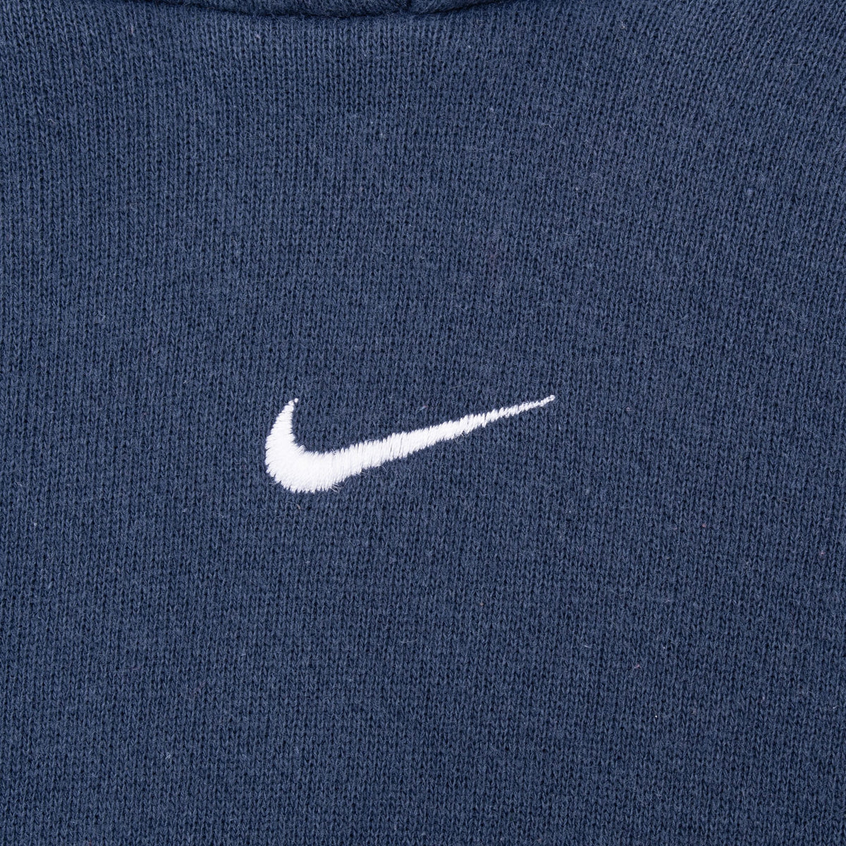 Close-up of white embroidered Nike Swoosh centered on navy blue hoodie chest