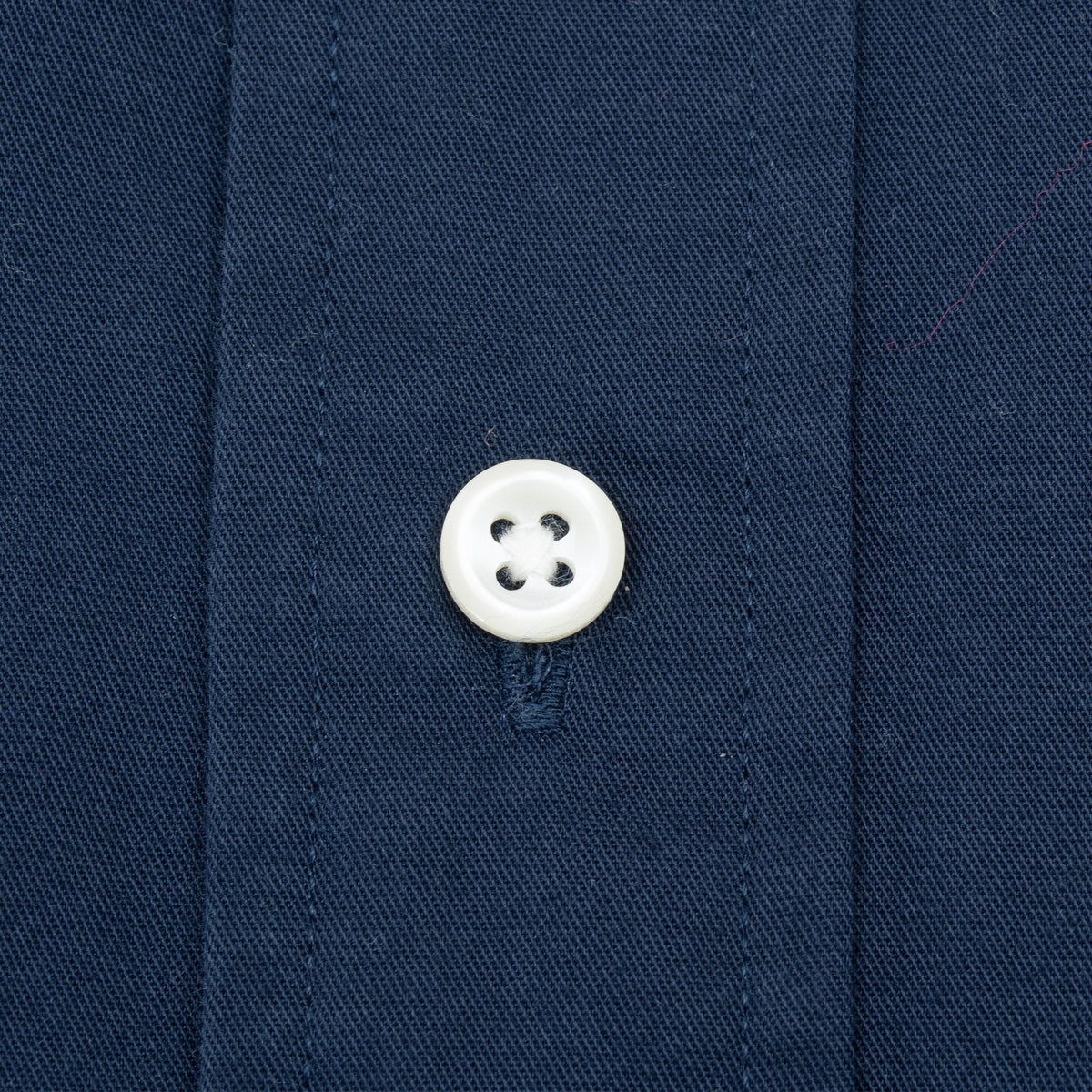 Close-up of a white four-hole button on the navy shirt placket