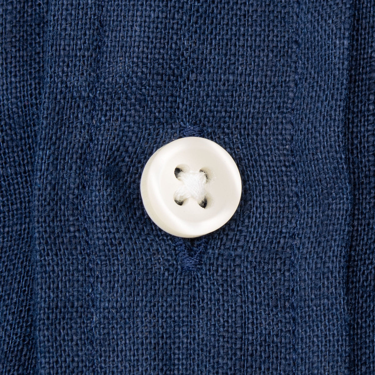 Close-up of contrasting white button and stitching on navy linen fabric