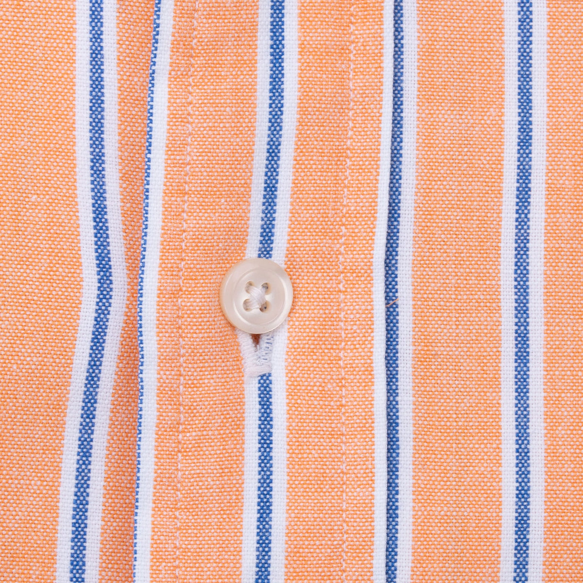 Close-up of white front button and stitching on peach, blue and white striped fabric