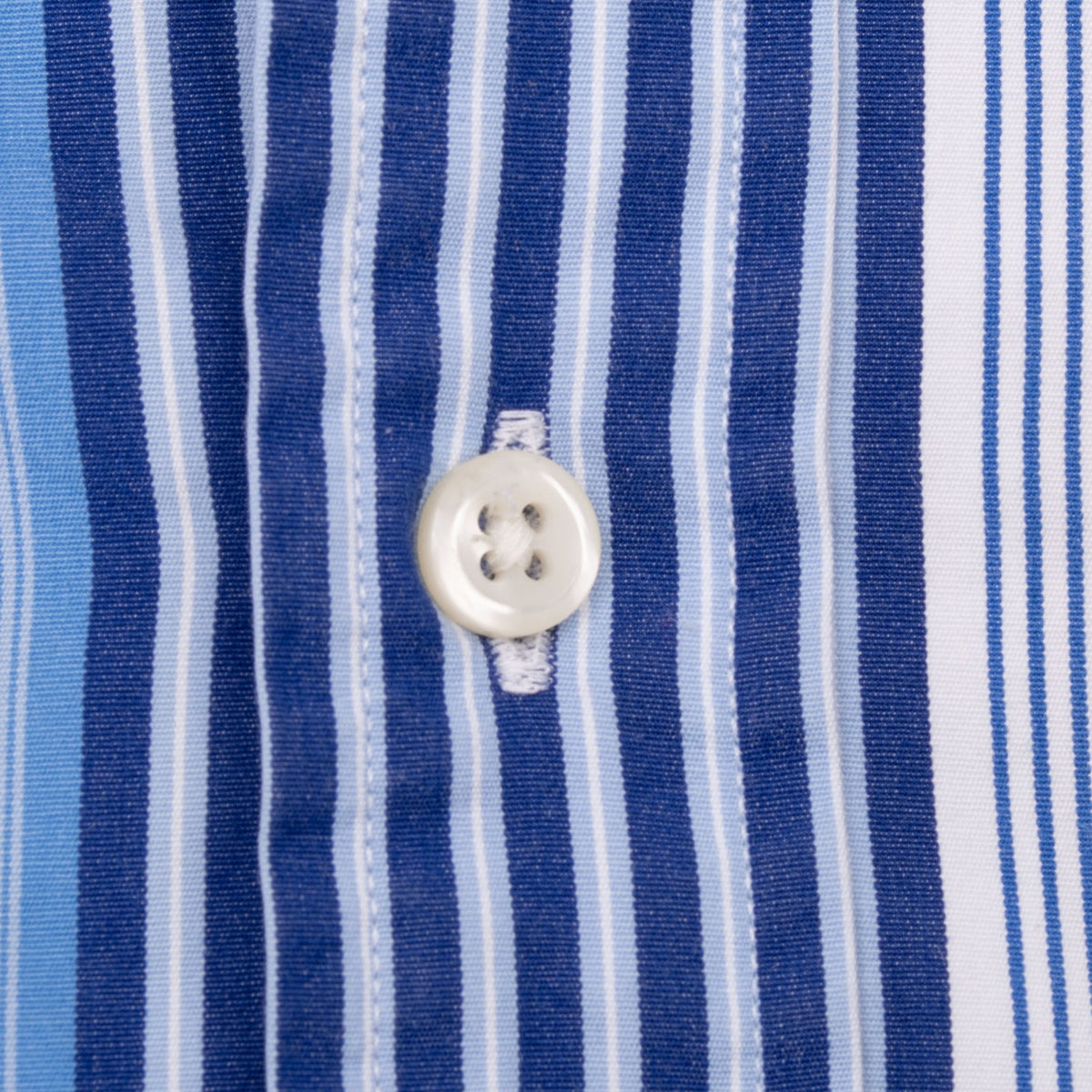 White front button and buttonhole detail on blue and white striped fabric