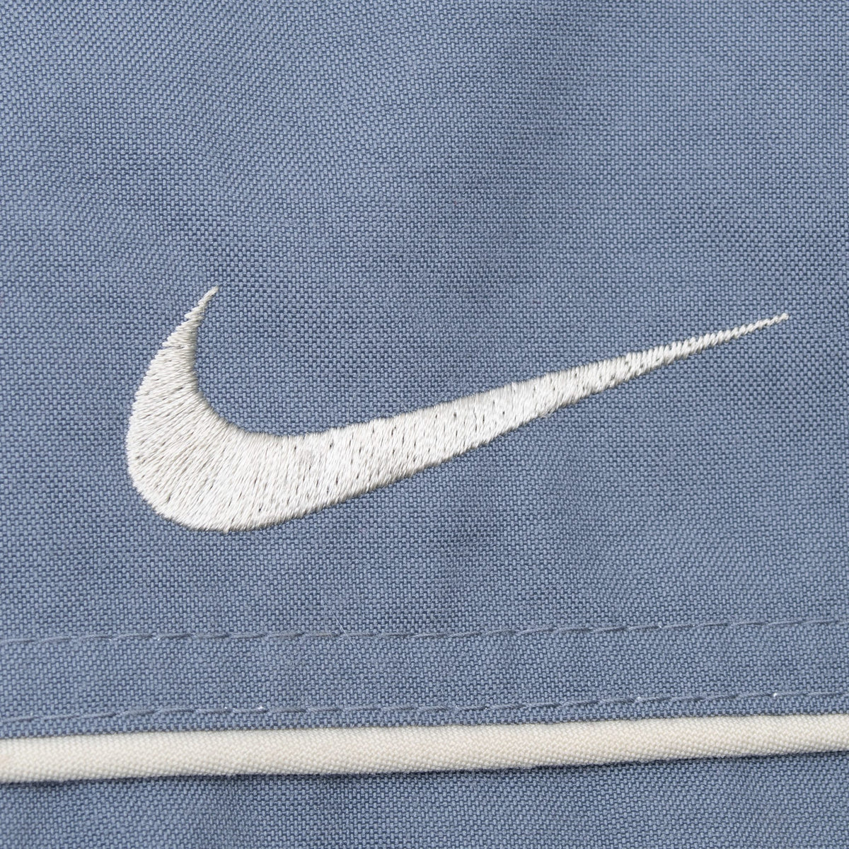 Close-up of white embroidered Nike Swoosh and contrast piping on grey fabric