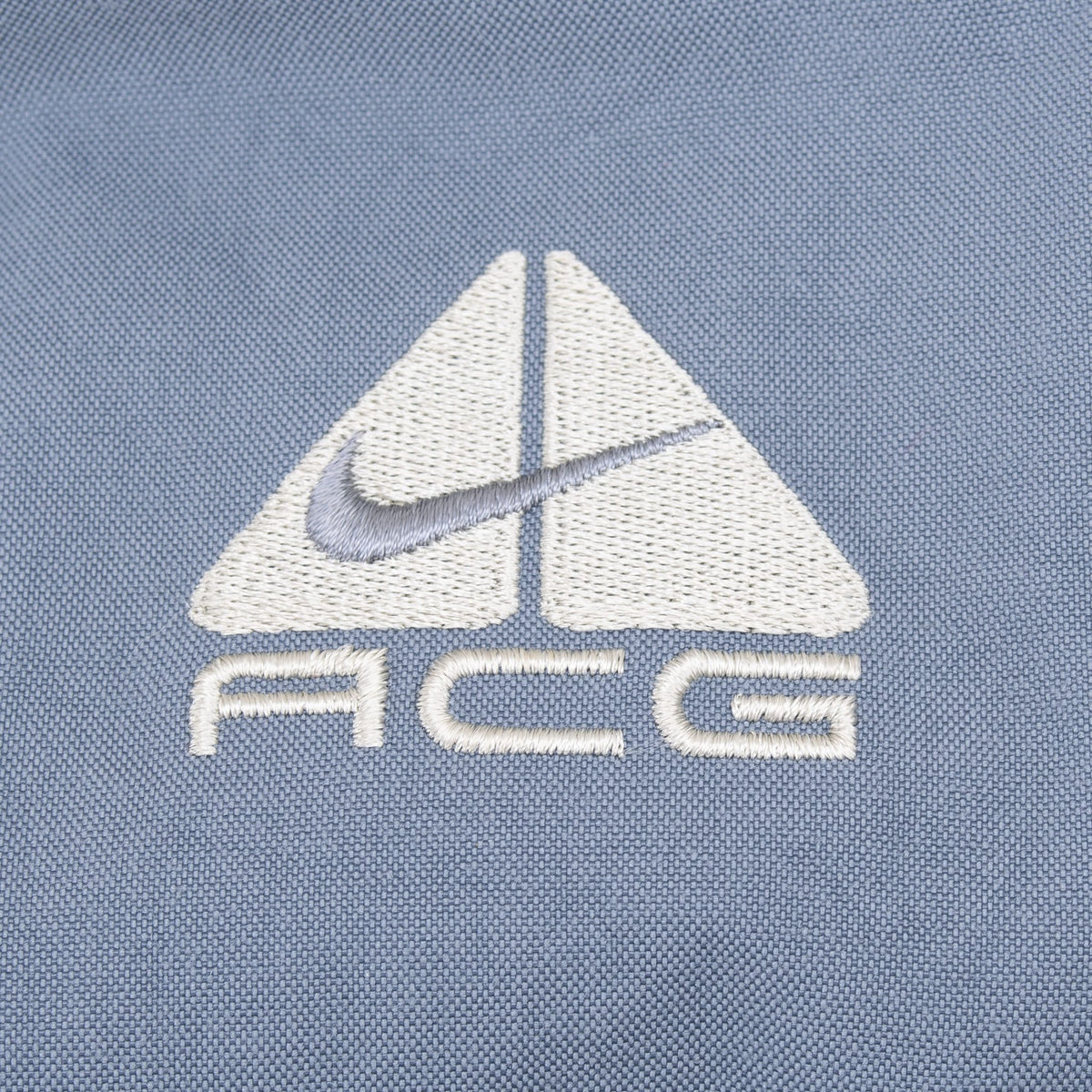 Close-up of white and grey embroidered Nike ACG logo on grey fabric