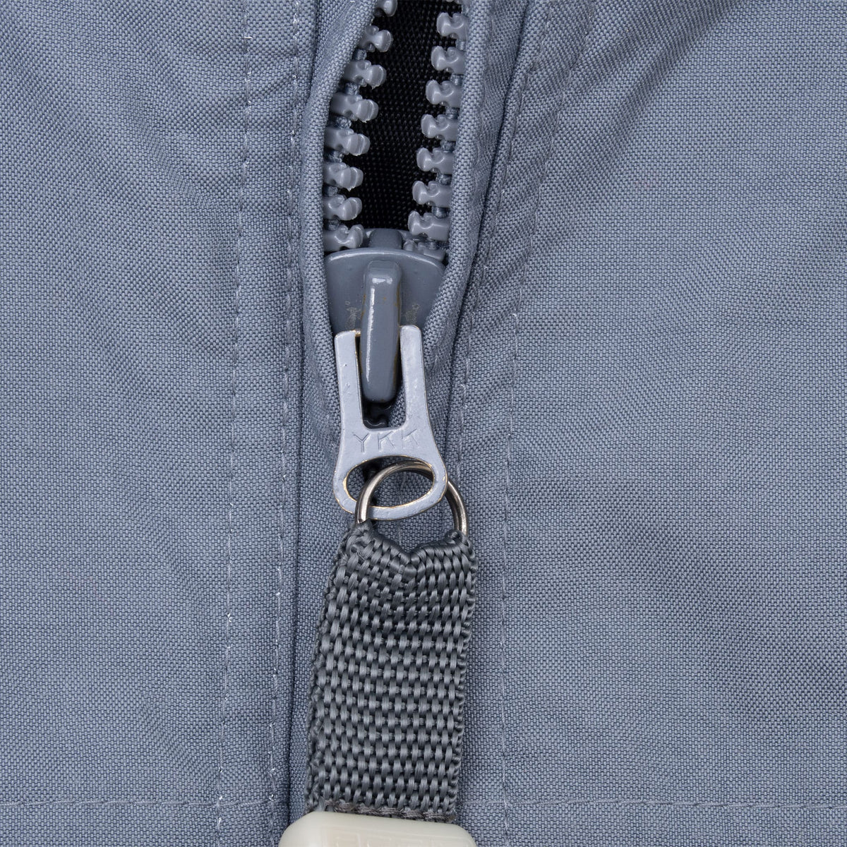 Close-up of grey front zipper pull with woven tab on the Nike ACG windbreaker