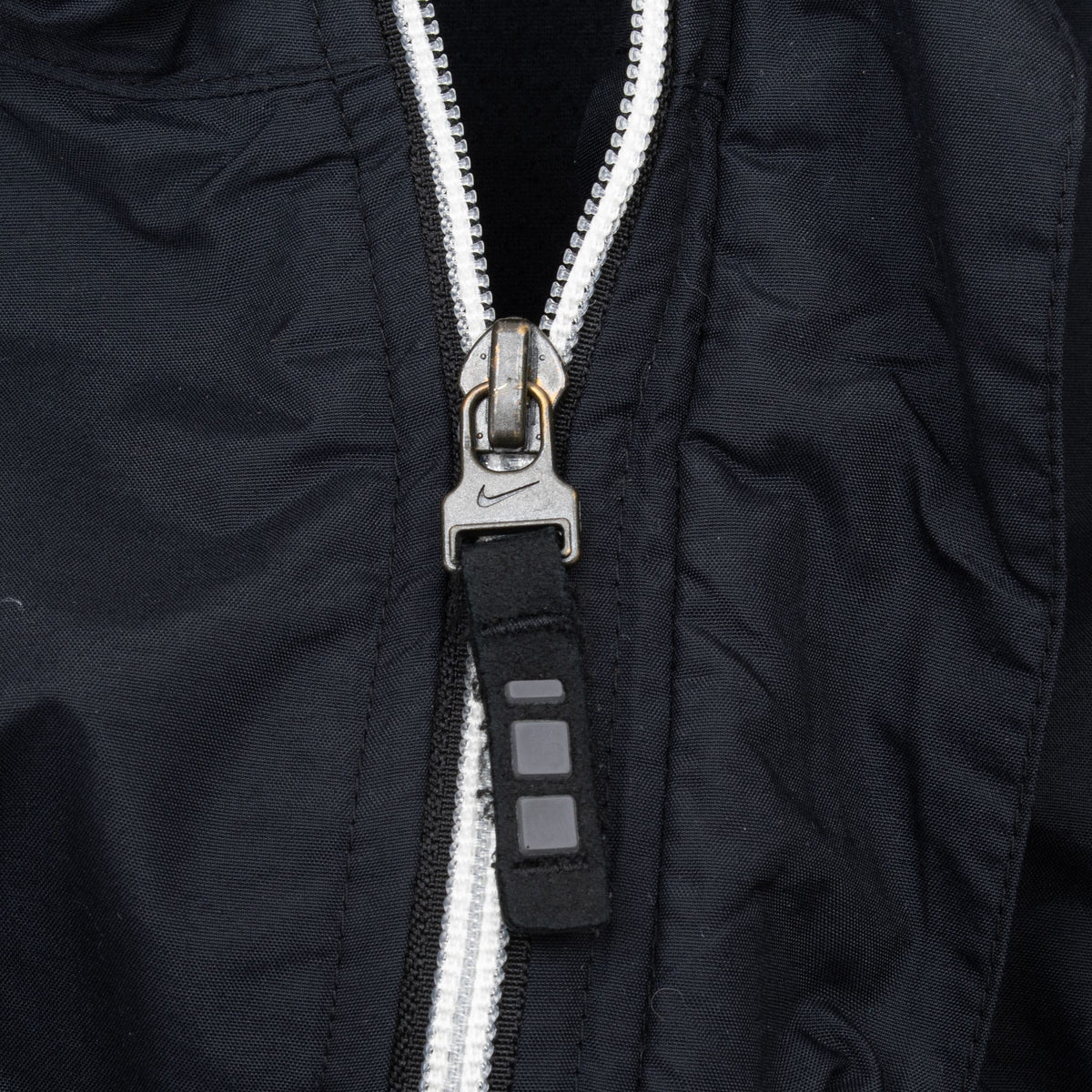 Close-up of Nike-branded metal zipper pull on black windbreaker jacket
