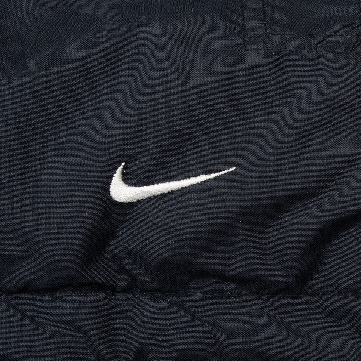 Close-up of white embroidered Nike Swoosh on black windbreaker fabric