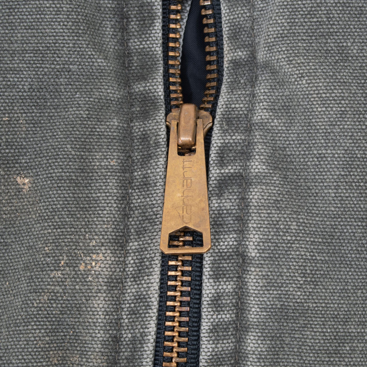 Close-up of brass-tone Carhartt zipper pull and faded green fabric