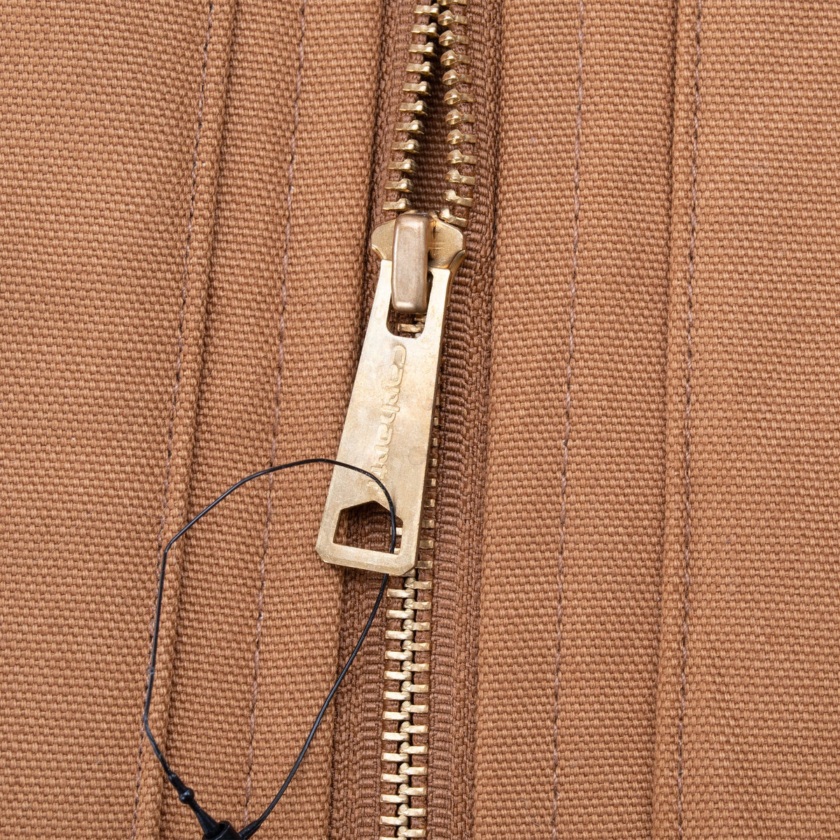Close-up of brass Carhartt zipper pull on brown vest