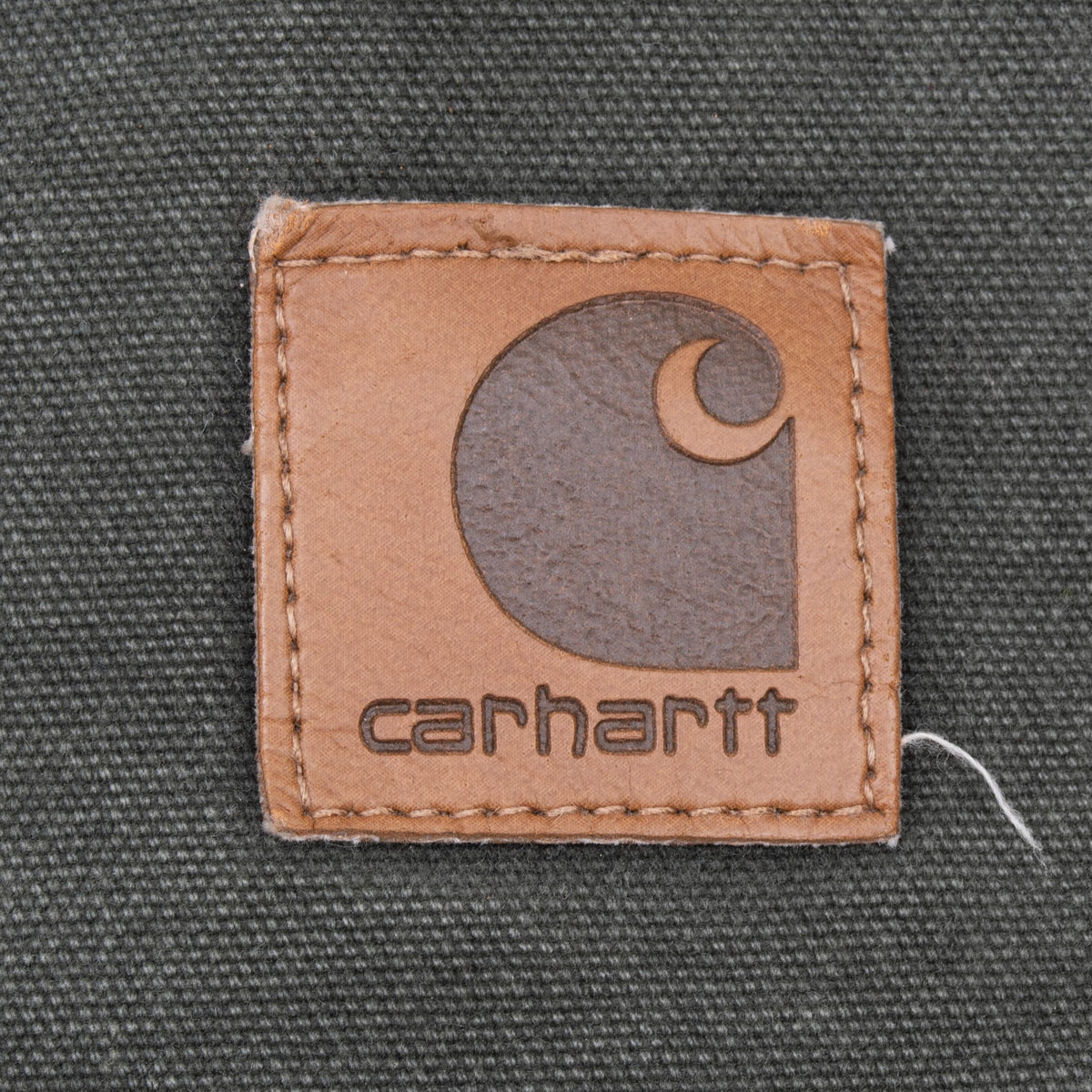Close-up of tan Carhartt logo patch stitched on green chest pocket