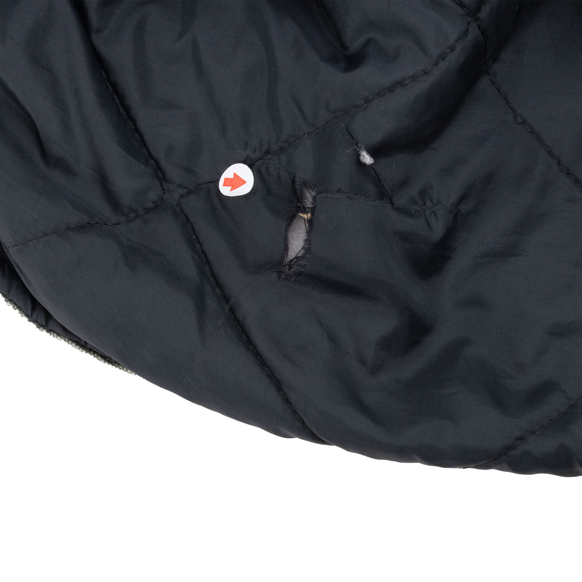 Close-up of a small tear in the black quilted lining near the hem, marked with an arrow