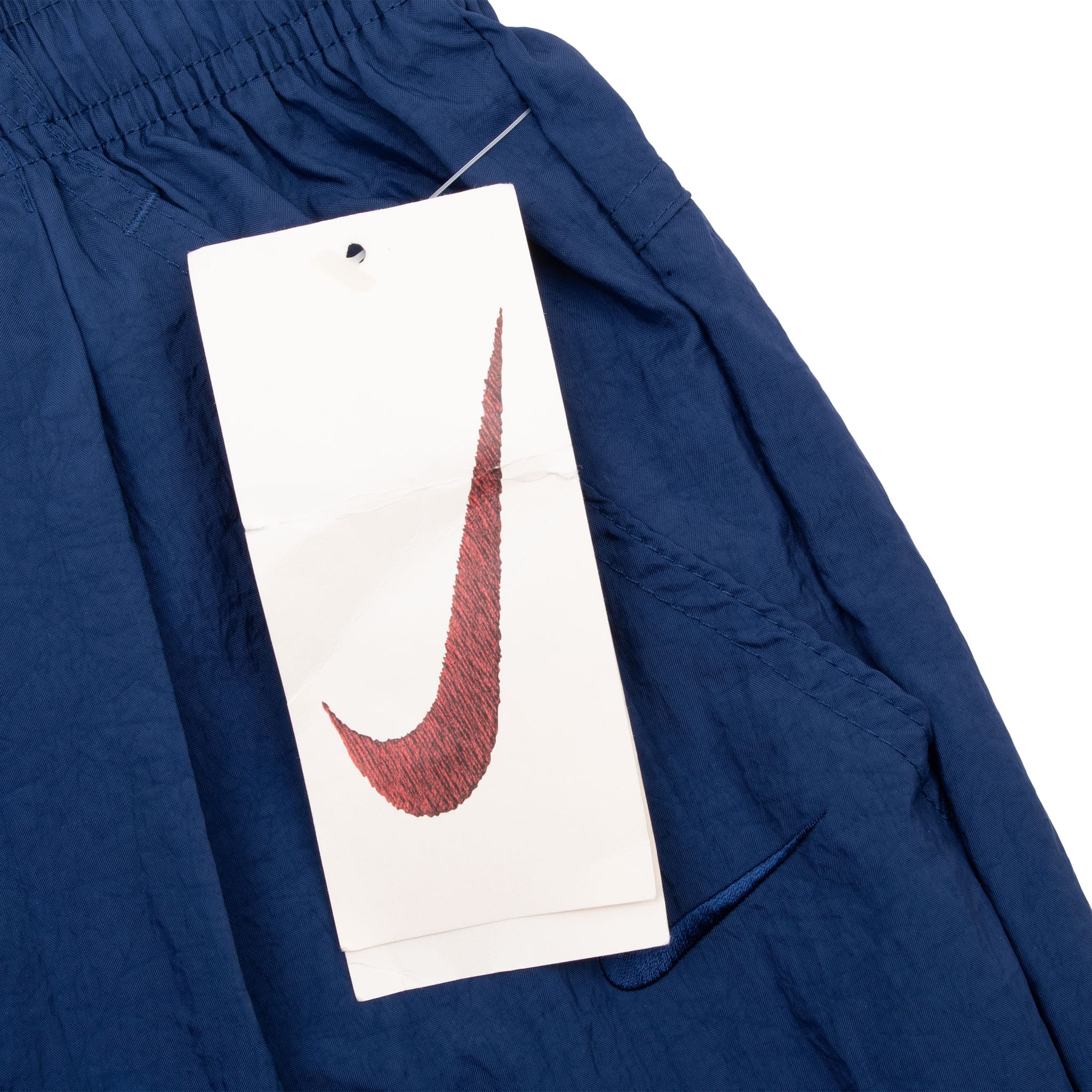 Nike Swoosh hangtag attached at the waistband of blue track pants