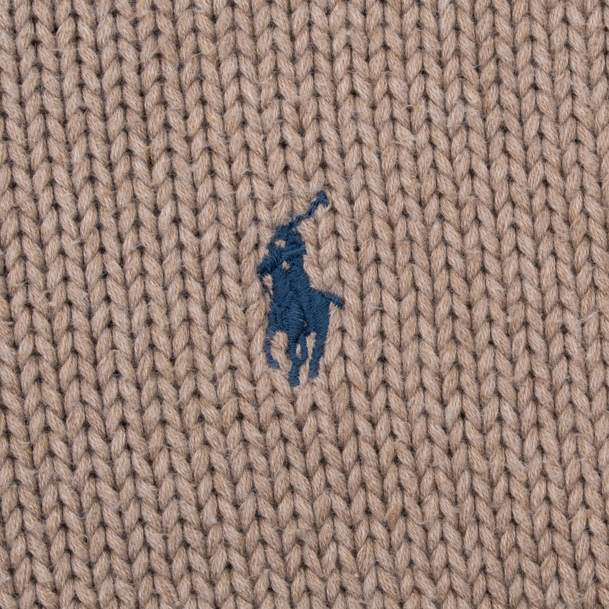 Close-up of navy Polo pony embroidery on beige knit fabric
