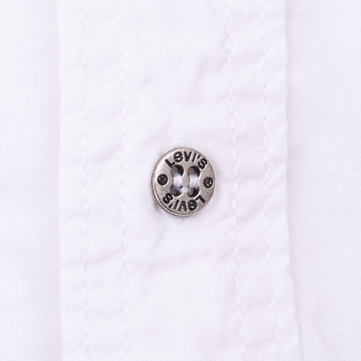 Close-up of Levi's-branded metal button on white shirt placket