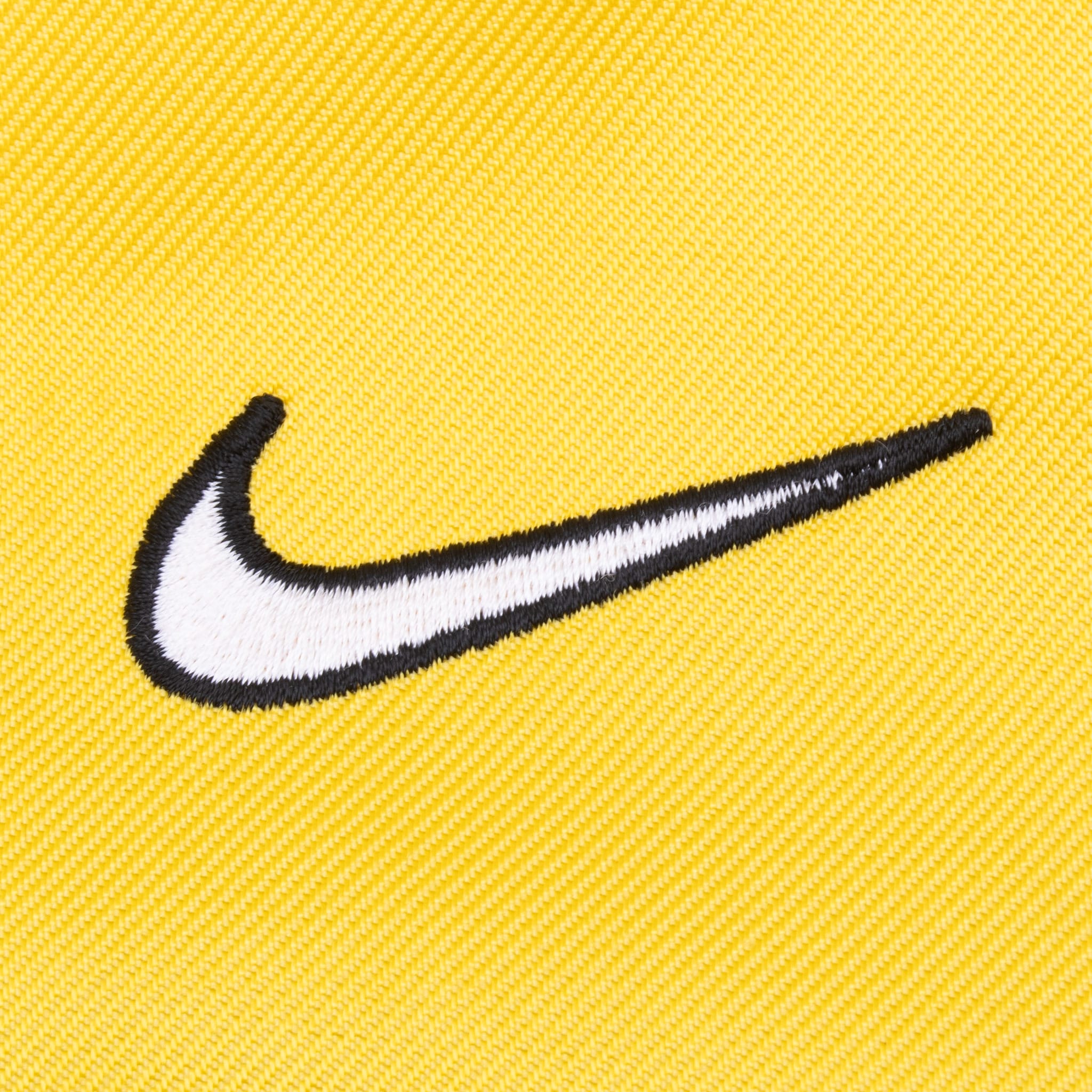 Close-up of white Nike Swoosh embroidery outlined in black on yellow chest