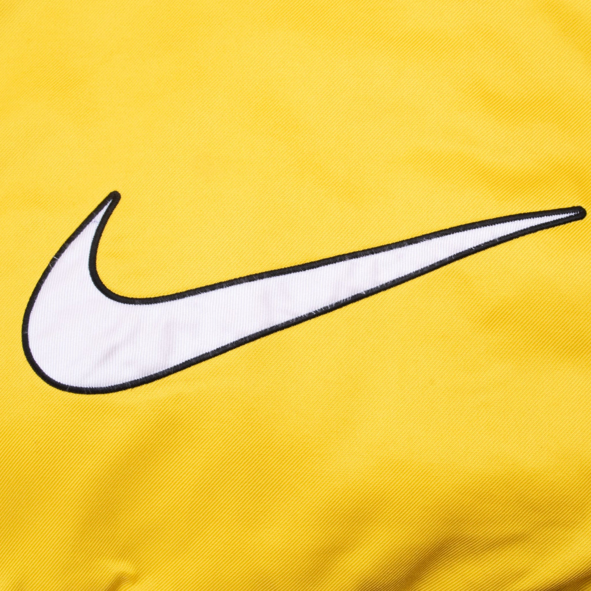 Close-up of large white Nike Swoosh applique outlined in black on yellow lower back