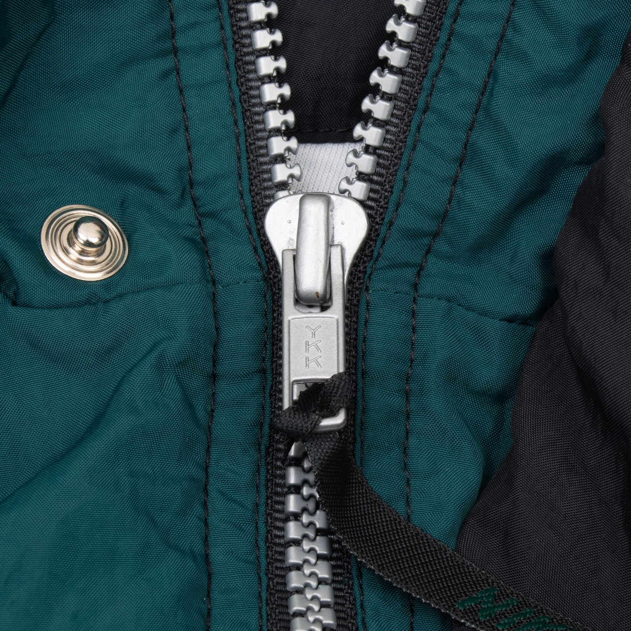 Close-up of front zipper and snap-fastened storm flap on green Nike windbreaker