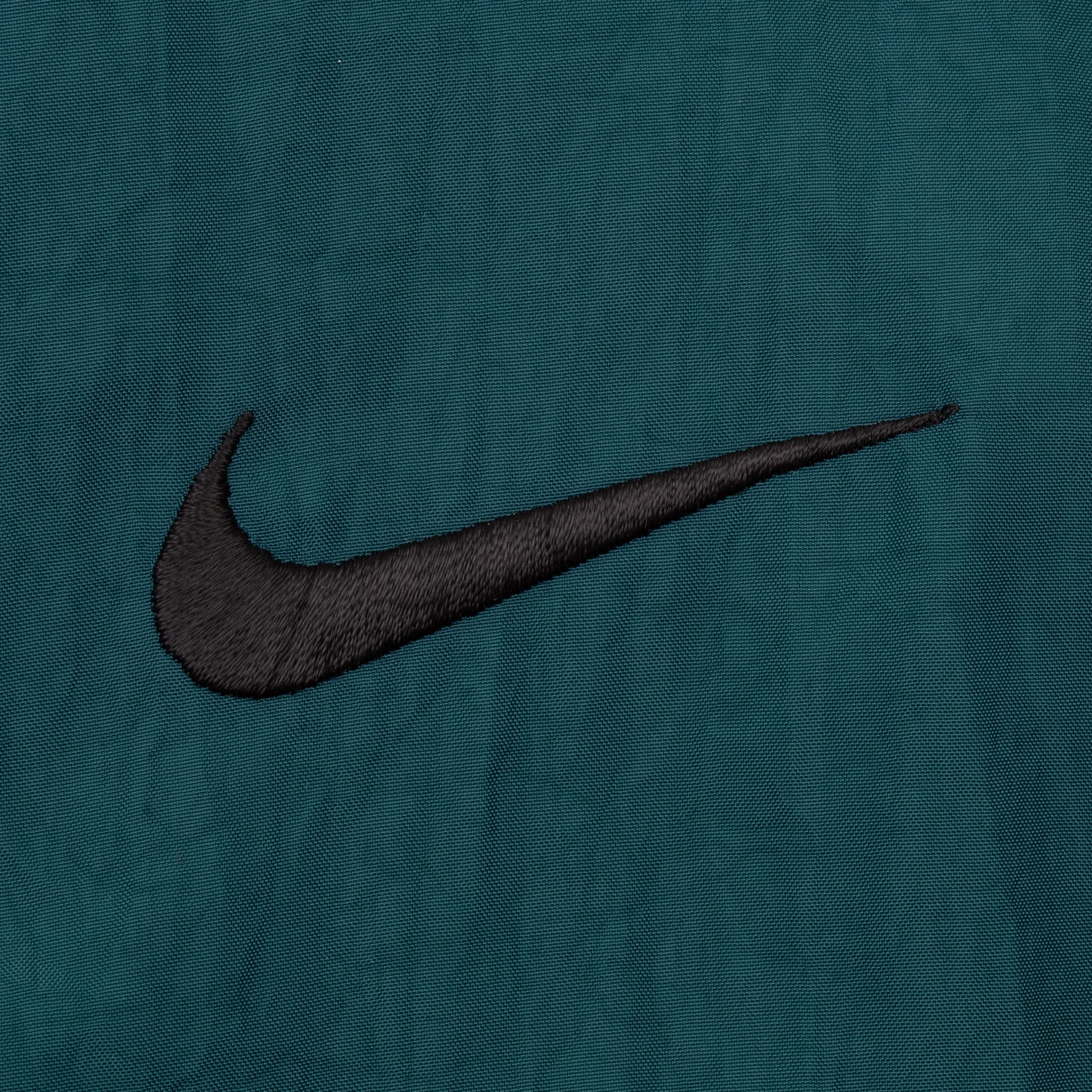 Close-up of black embroidered Nike Swoosh on green chest fabric