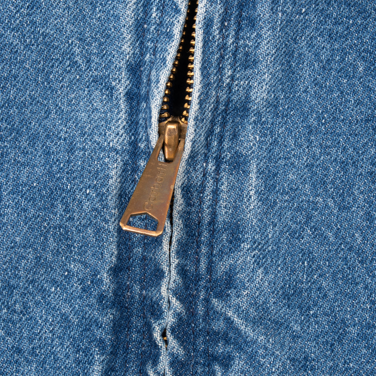Close-up of Carhartt-branded metal zipper pull on blue denim jacket