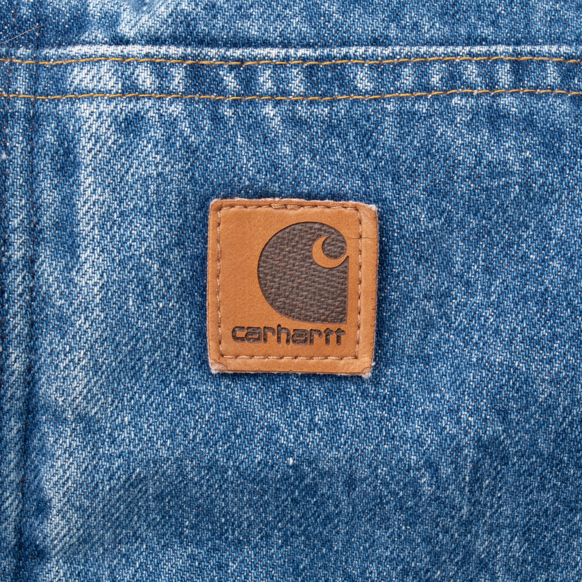 Close-up of brown Carhartt logo patch on blue denim pocket