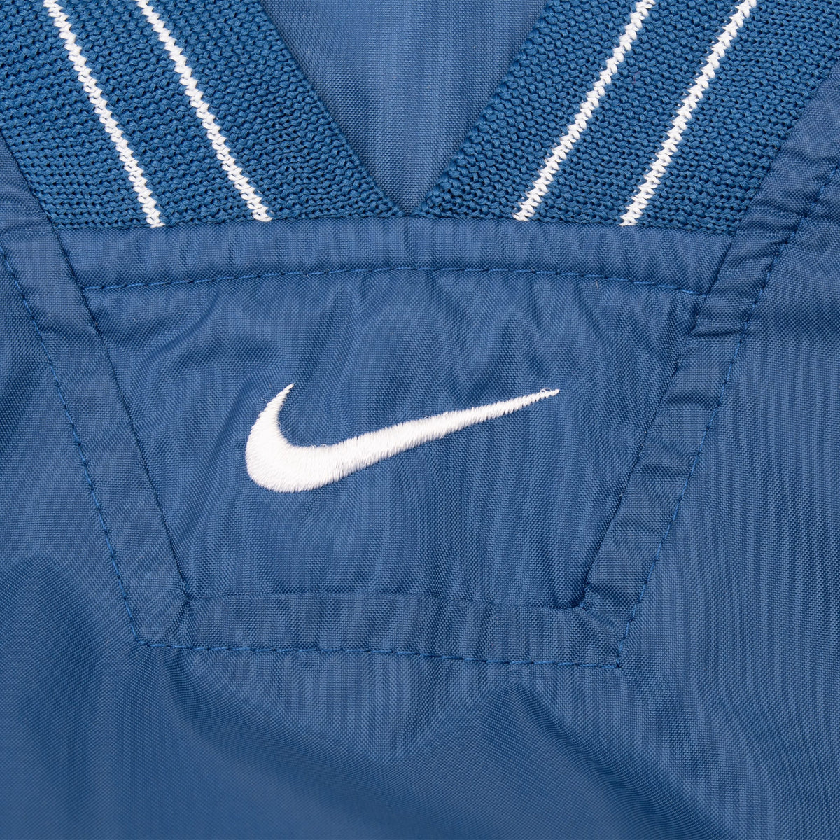 Close-up of white embroidered Nike Swoosh below the blue and white striped V-neck collar