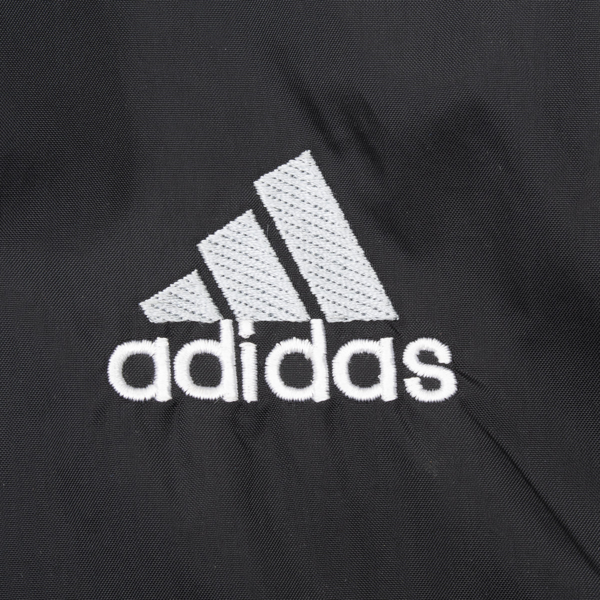 Close-up of white embroidered Adidas chest logo on black fabric