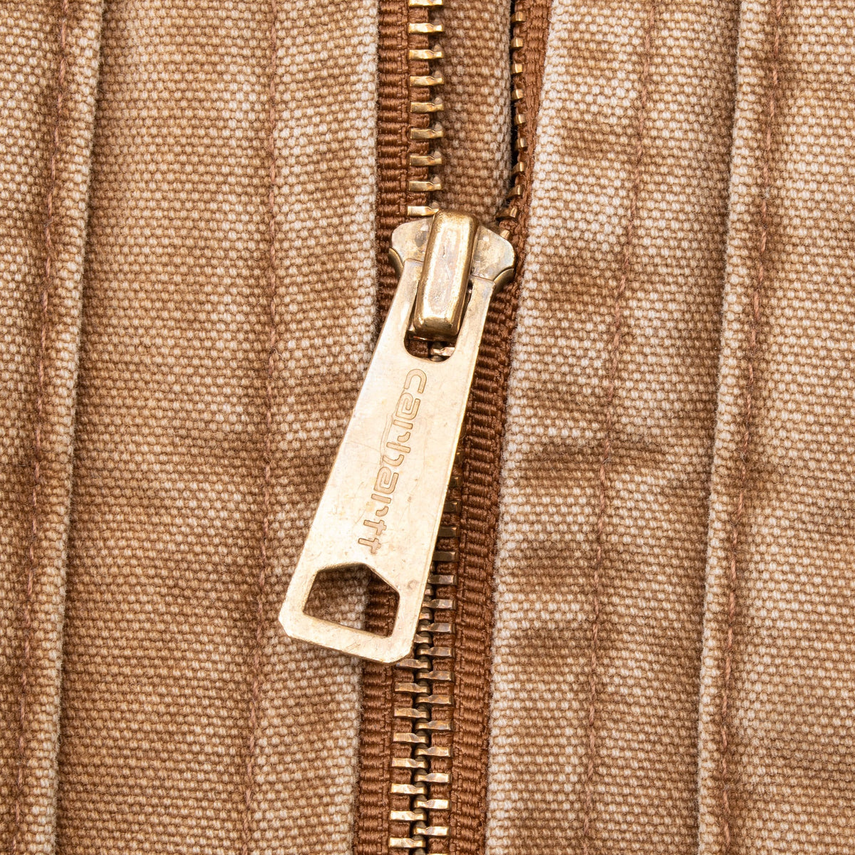Close-up of Carhartt-engraved metal zipper pull on brown fabric