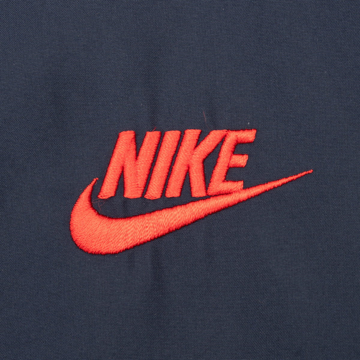 Close-up of red Nike Swoosh embroidery on navy windbreaker