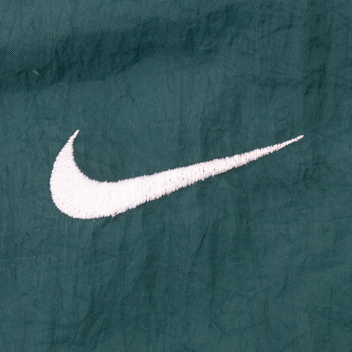 Close-up of white embroidered Nike Swoosh on green fabric
