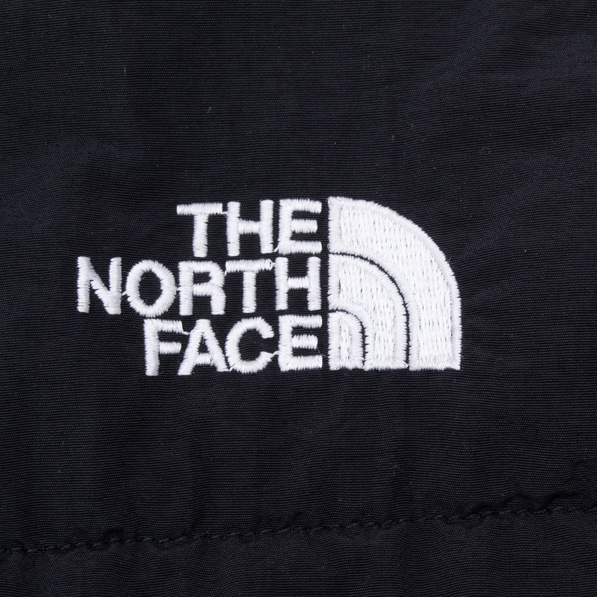 Close-up of white The North Face logo embroidery on black jacket panel
