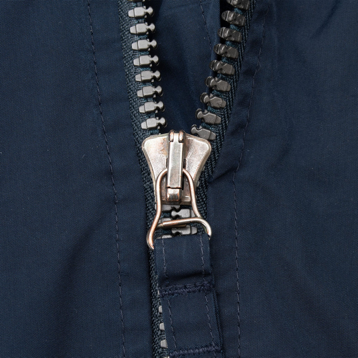 Close-up of the navy windbreaker's metal front zipper and fabric pull tab