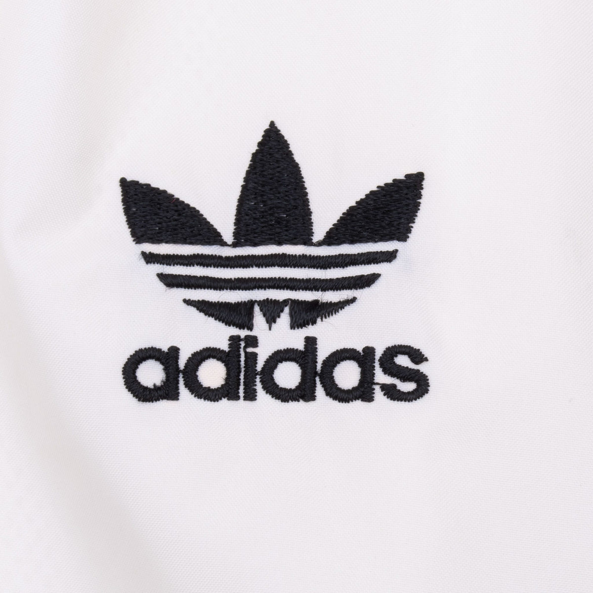 Close-up of black Adidas Trefoil logo embroidered on the white chest panel