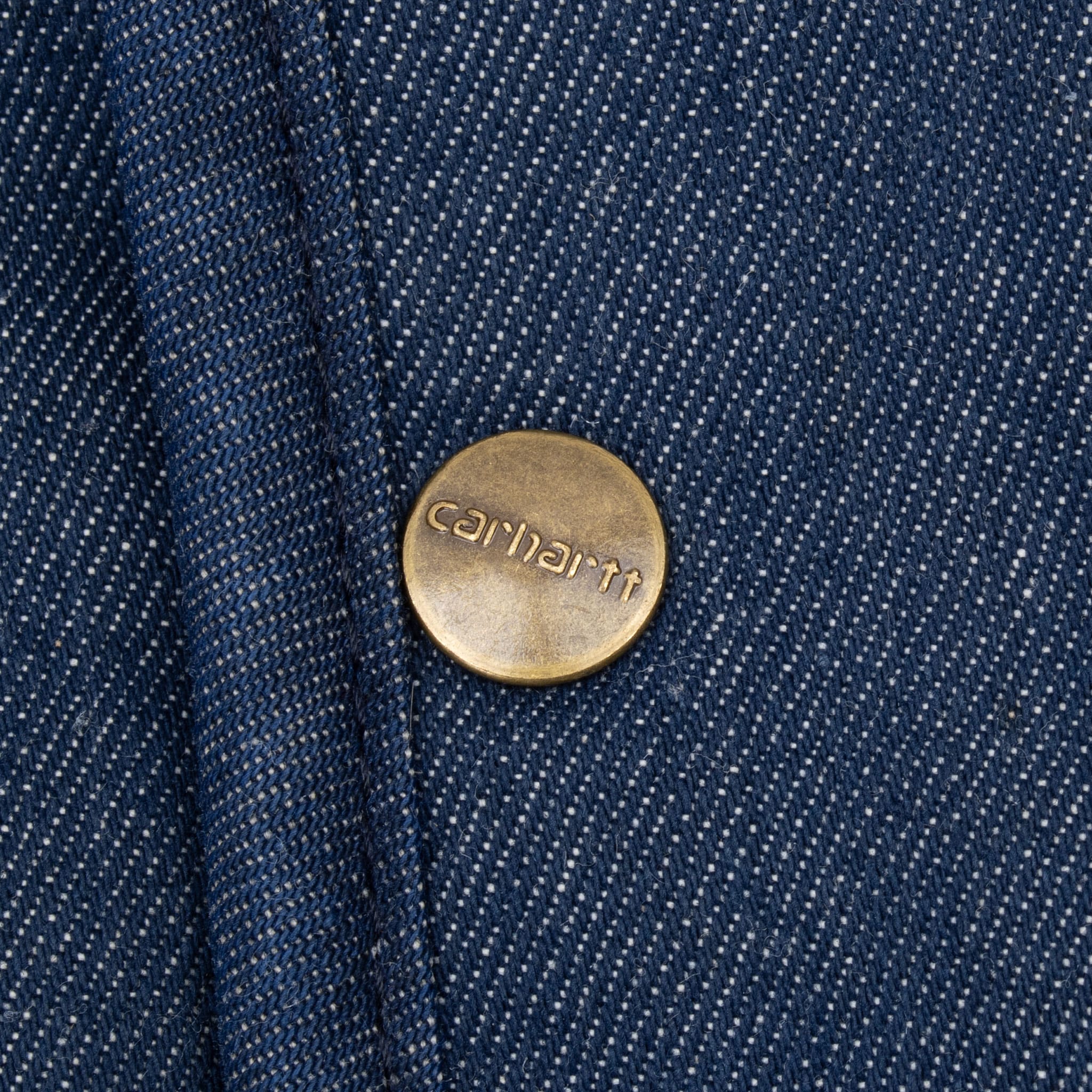 Close-up of brass-tone Carhartt snap on dark blue denim