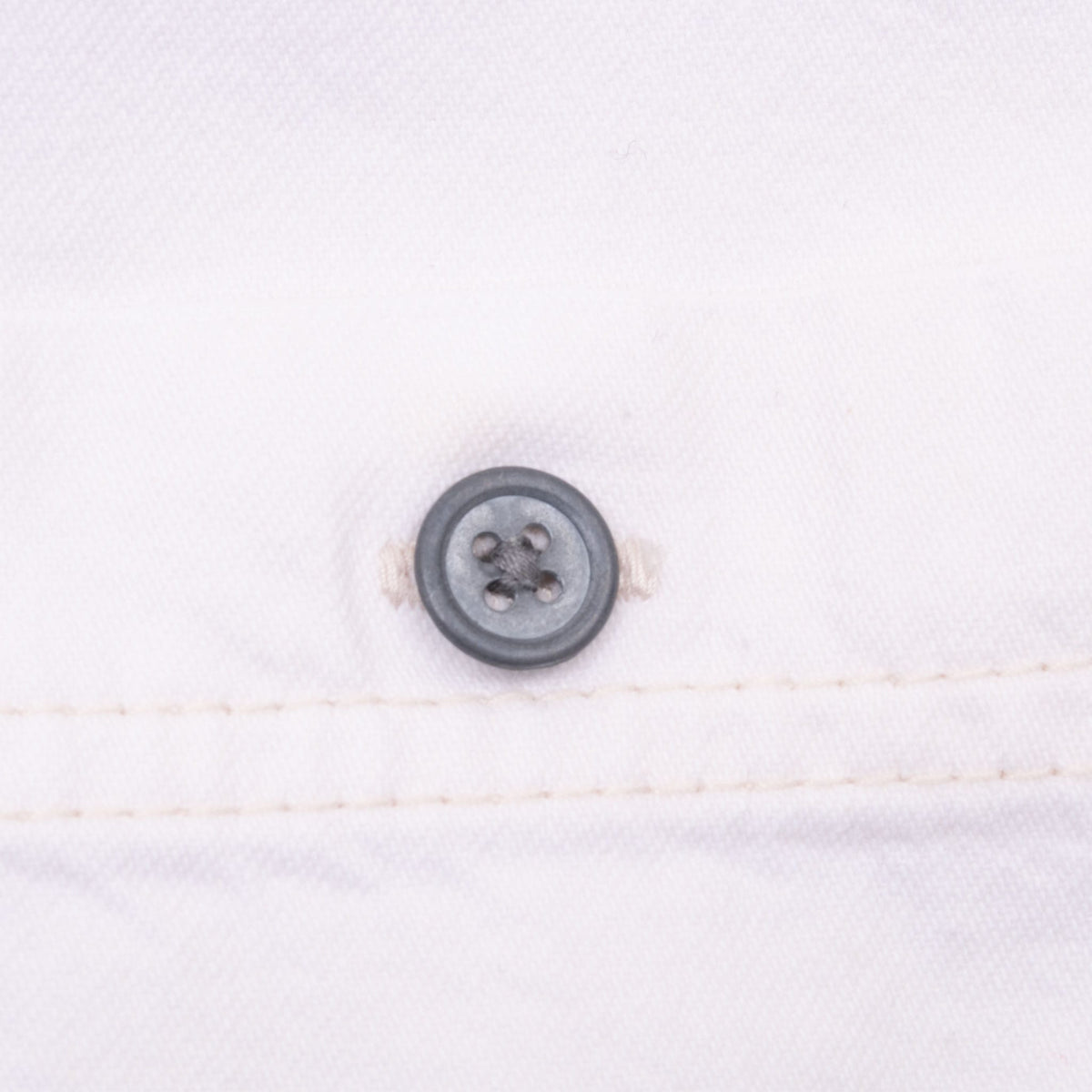 Close-up of dark four-hole button and stitching on white denim shirt
