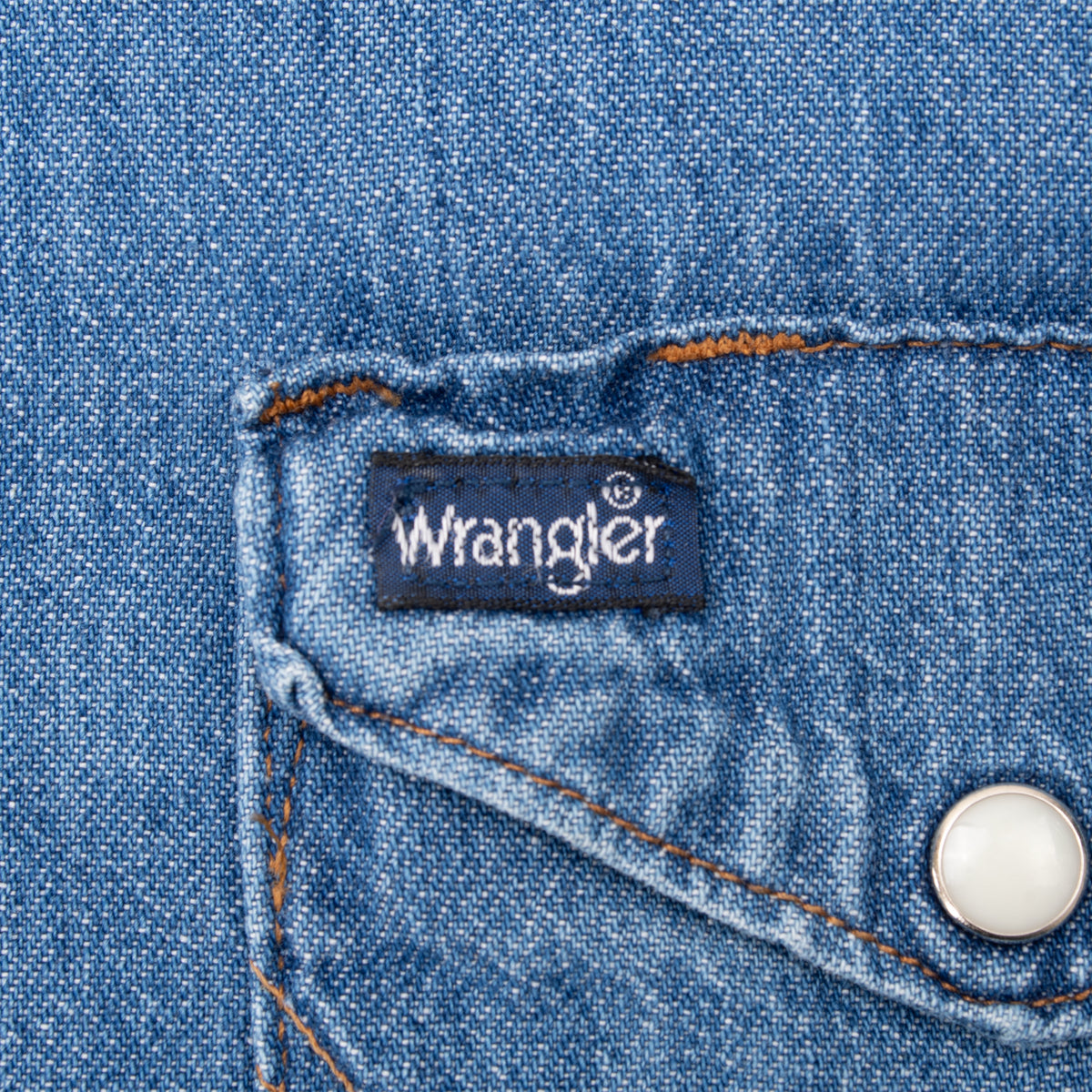 Wrangler logo tag and white pearl snap detail on blue denim chest pocket