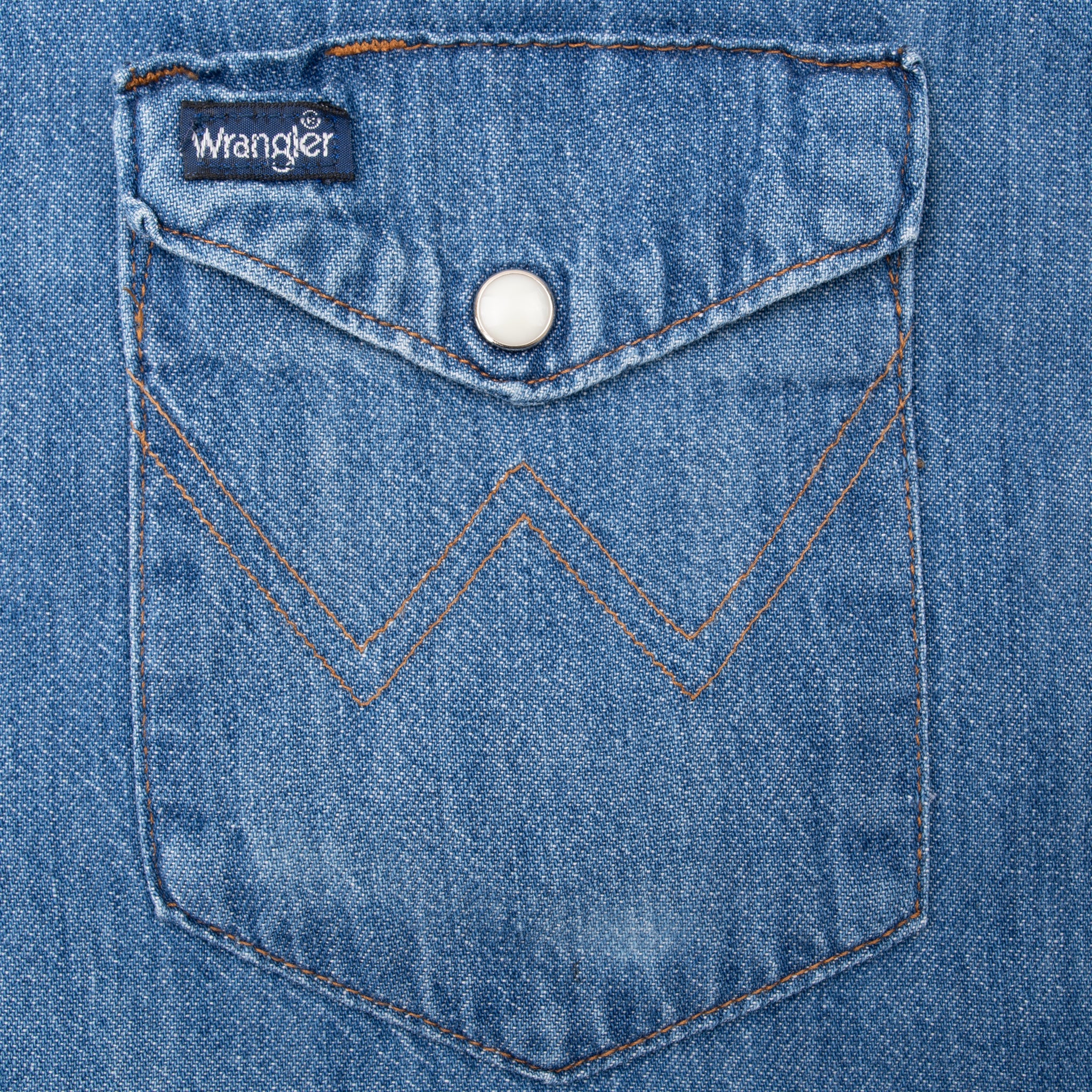 Blue denim chest pocket with Wrangler tag, white pearl snap, and W stitching