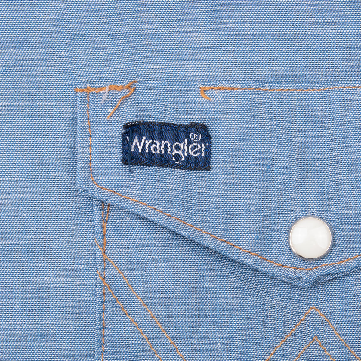 Wrangler chest pocket label, pearl snap, and orange stitching detail