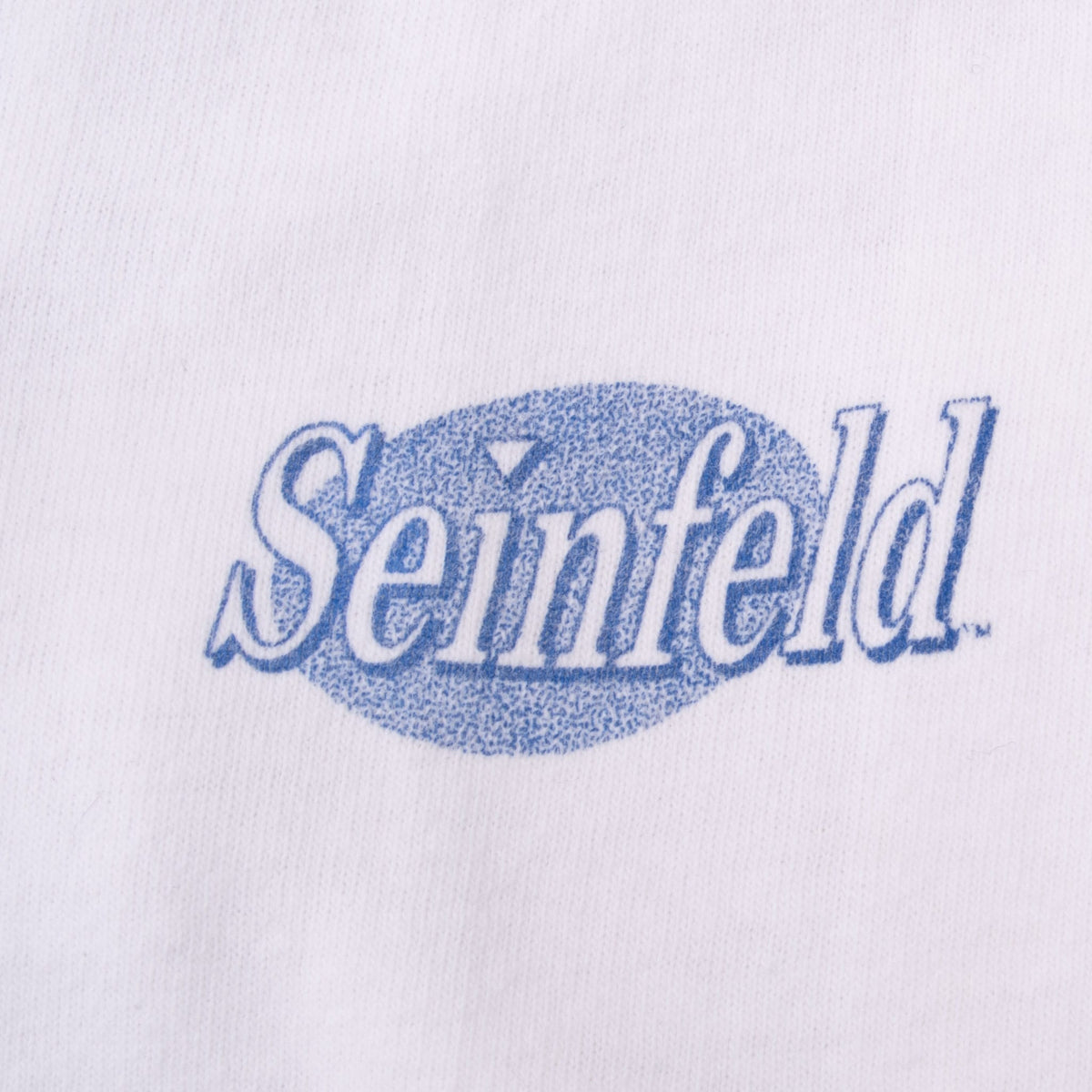Close-up of blue Seinfeld logo printed on white T-shirt sleeve