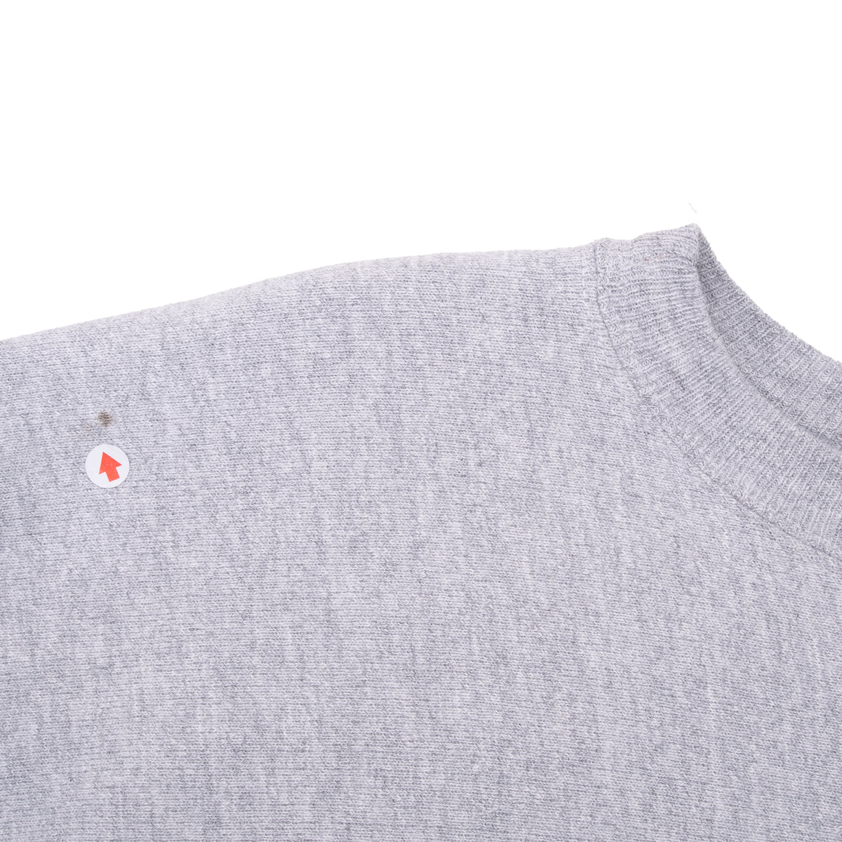 Close-up of grey sweatshirt shoulder and ribbed crew neck with a small spot indicated