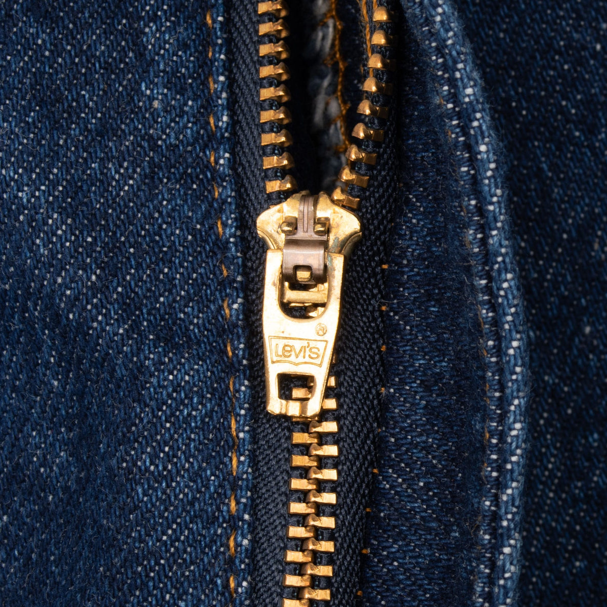 Close-up of the Levi's branded brass-tone zipper on dark indigo jeans