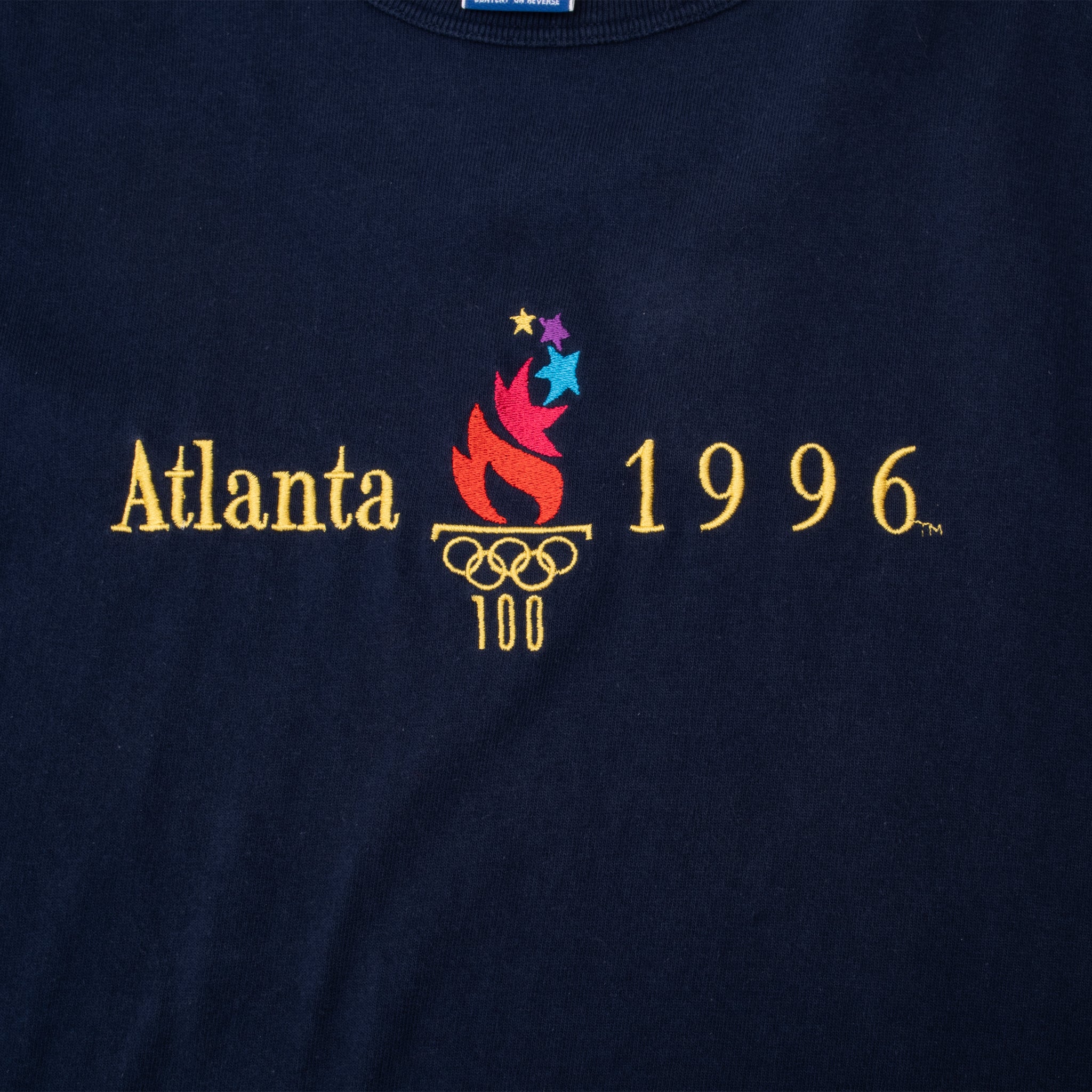 Close-up of embroidered Atlanta 1996 Olympics logo on navy Champion tee