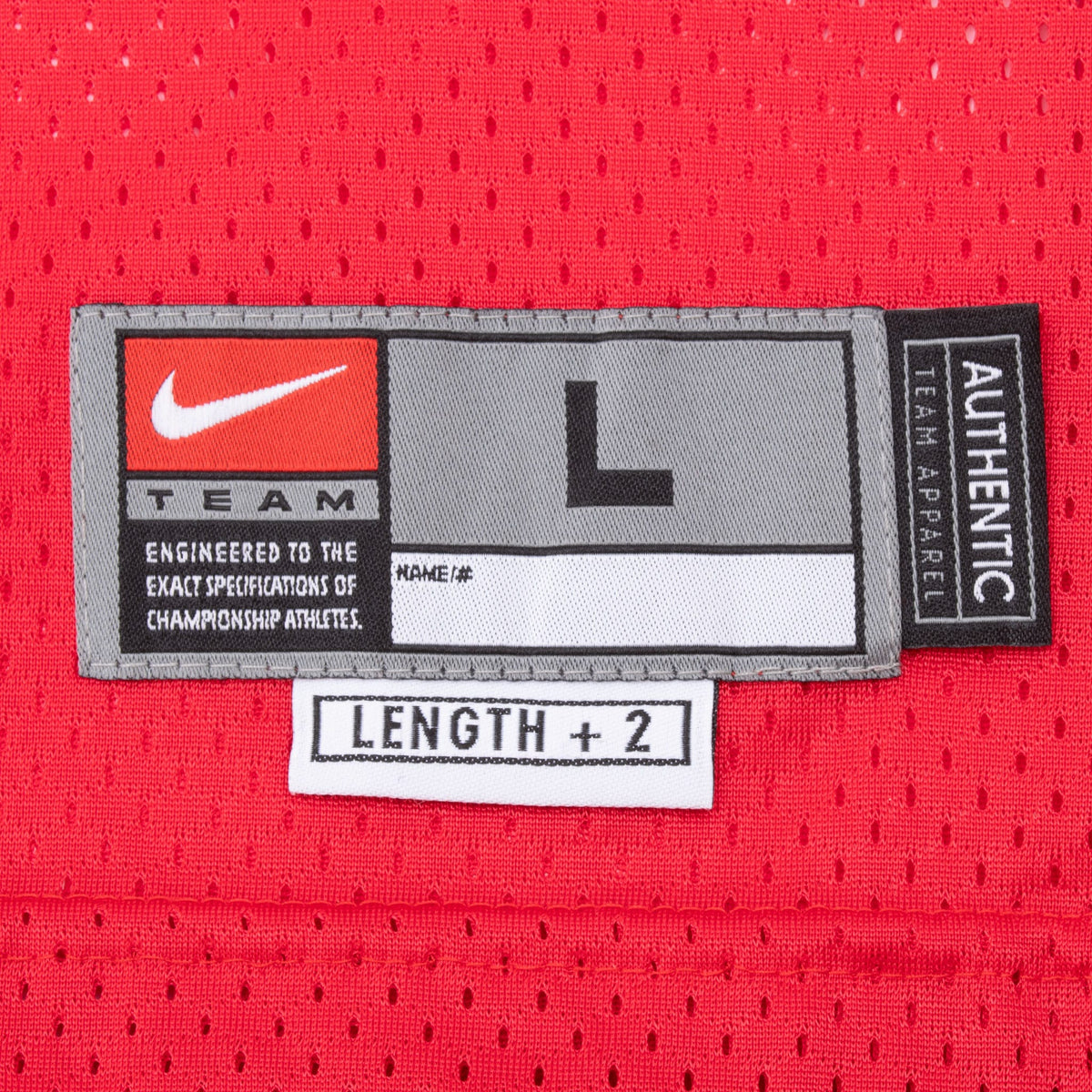 Close-up of Nike Team size L jock tag and Length +2 label on red mesh fabric
