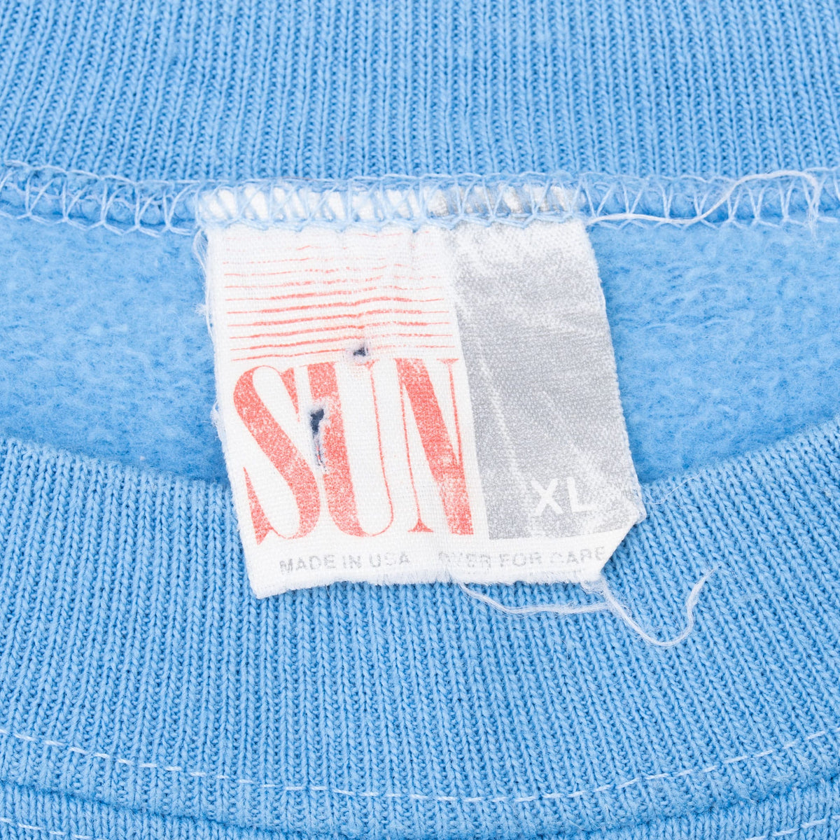 Close-up of SUN neck tag marked XL and Made in USA inside blue UCLA sweatshirt