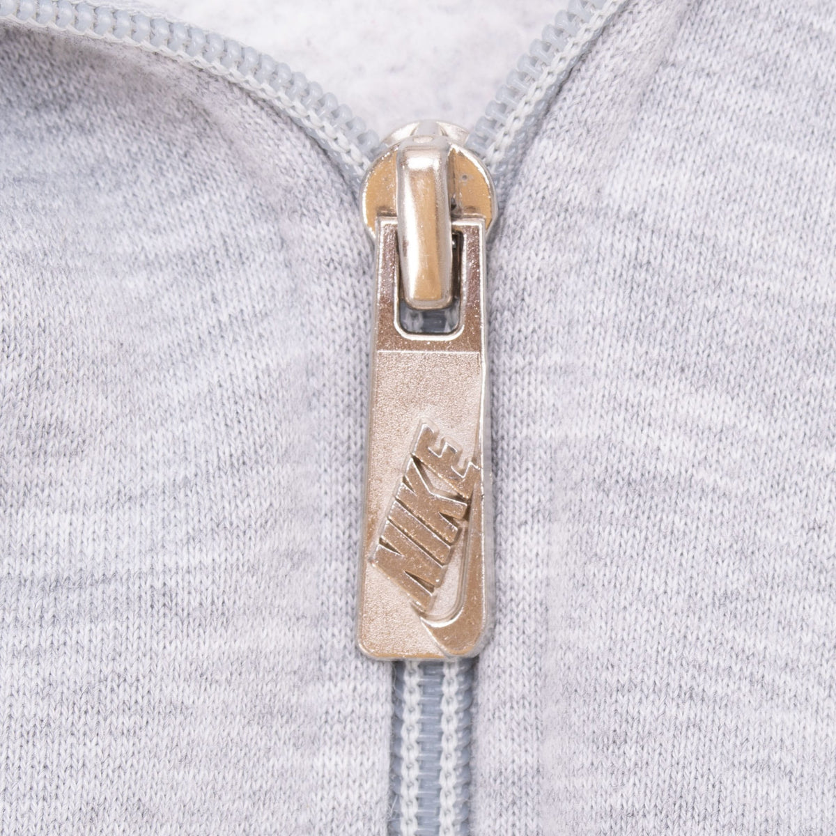 Close-up of Nike-branded metal zipper pull on grey hoodie