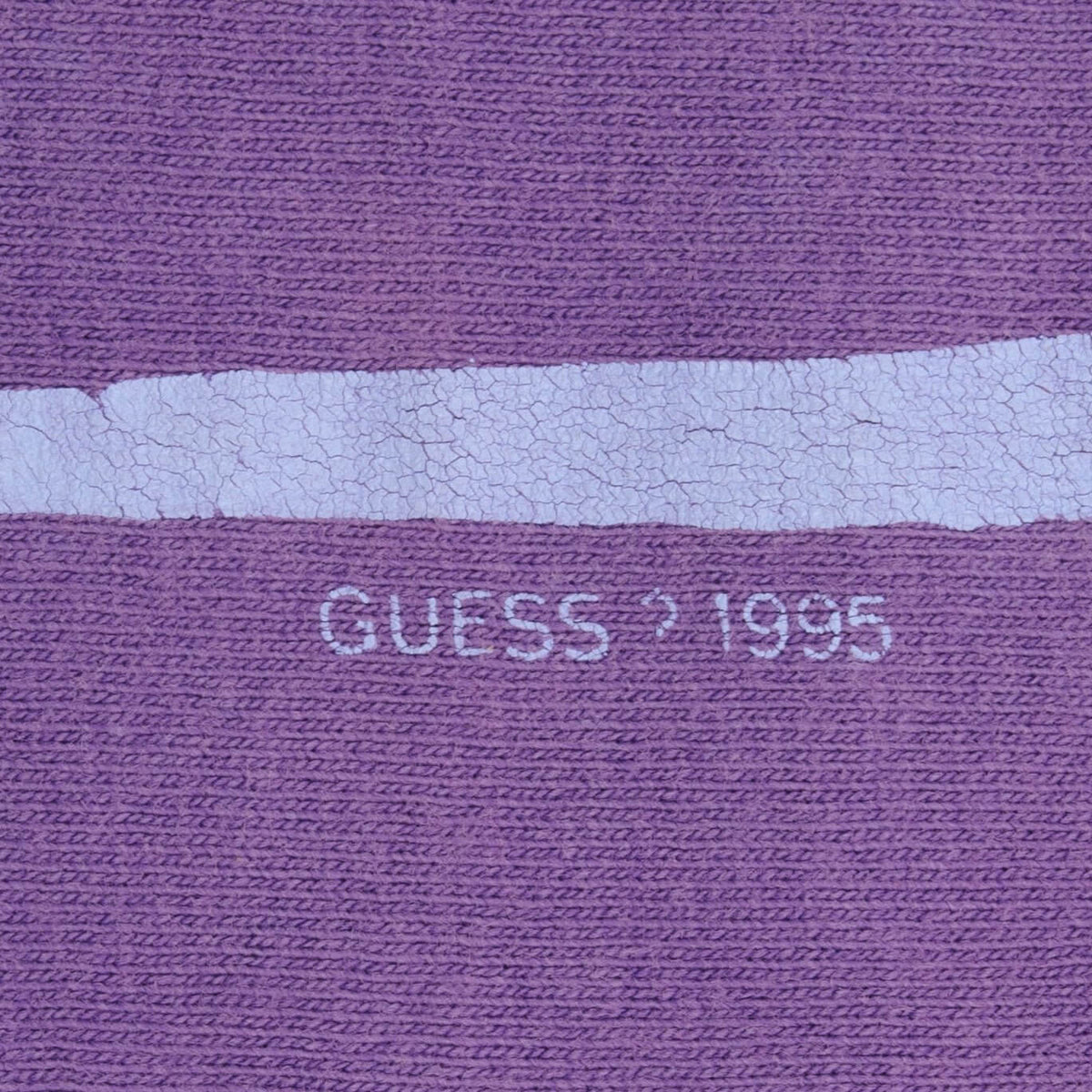 Close-up of cracked print and small Guess 1995 marking on purple fabric