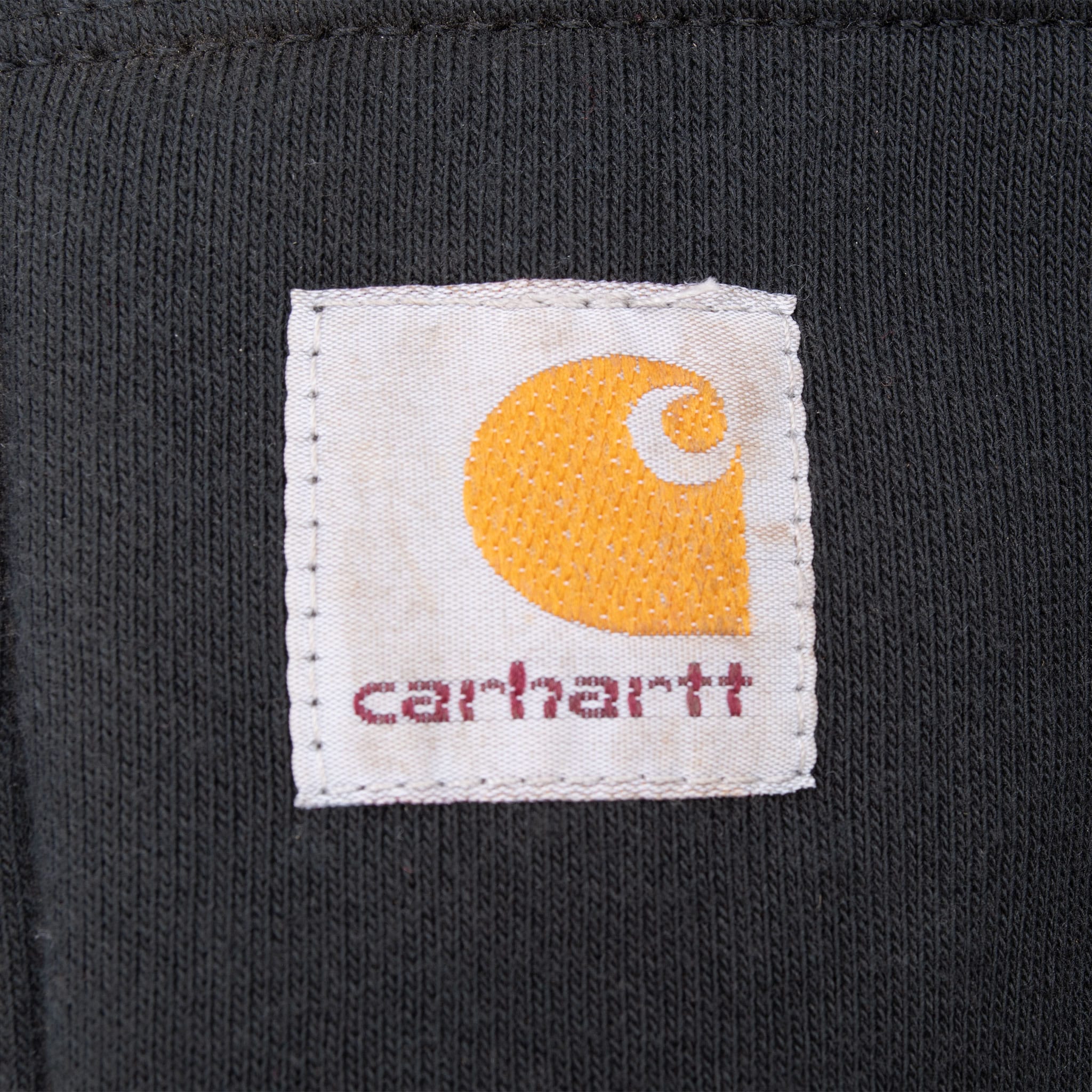 Close-up of woven Carhartt logo patch on black pouch pocket