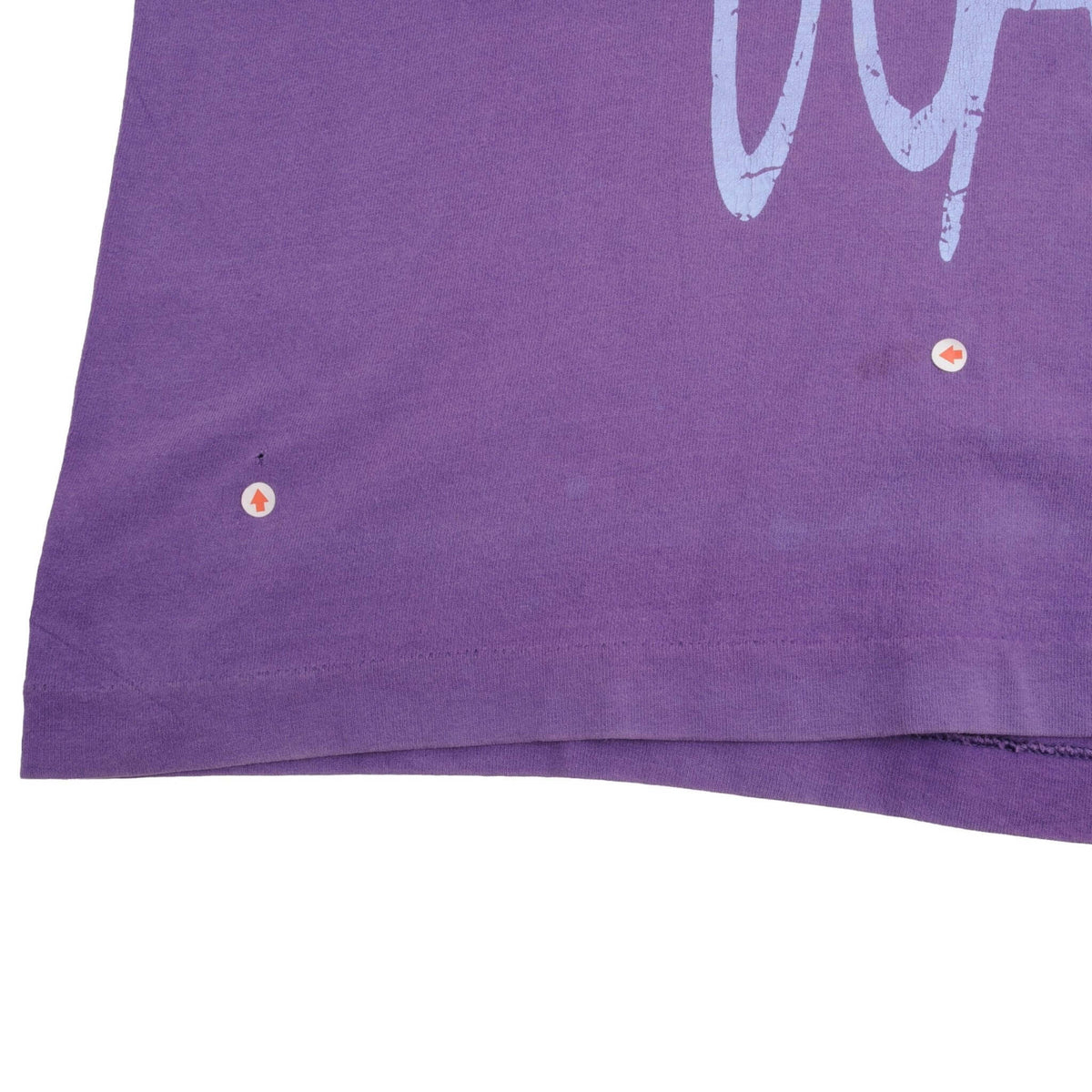 Lower front hem of purple Guess Jeans T-shirt with two marked small flaws