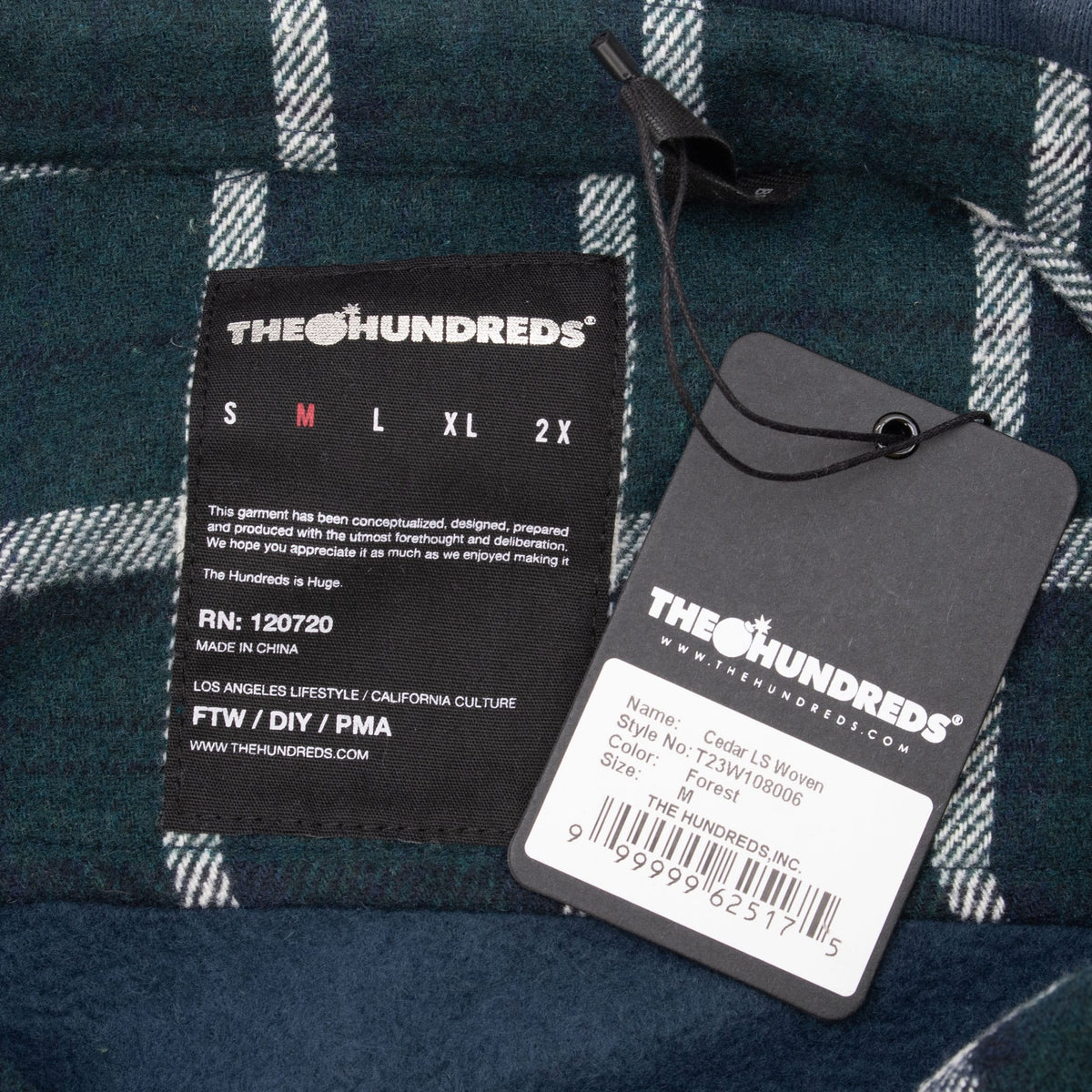 The Hundreds neck label with medium marked in red beside the attached product hangtag