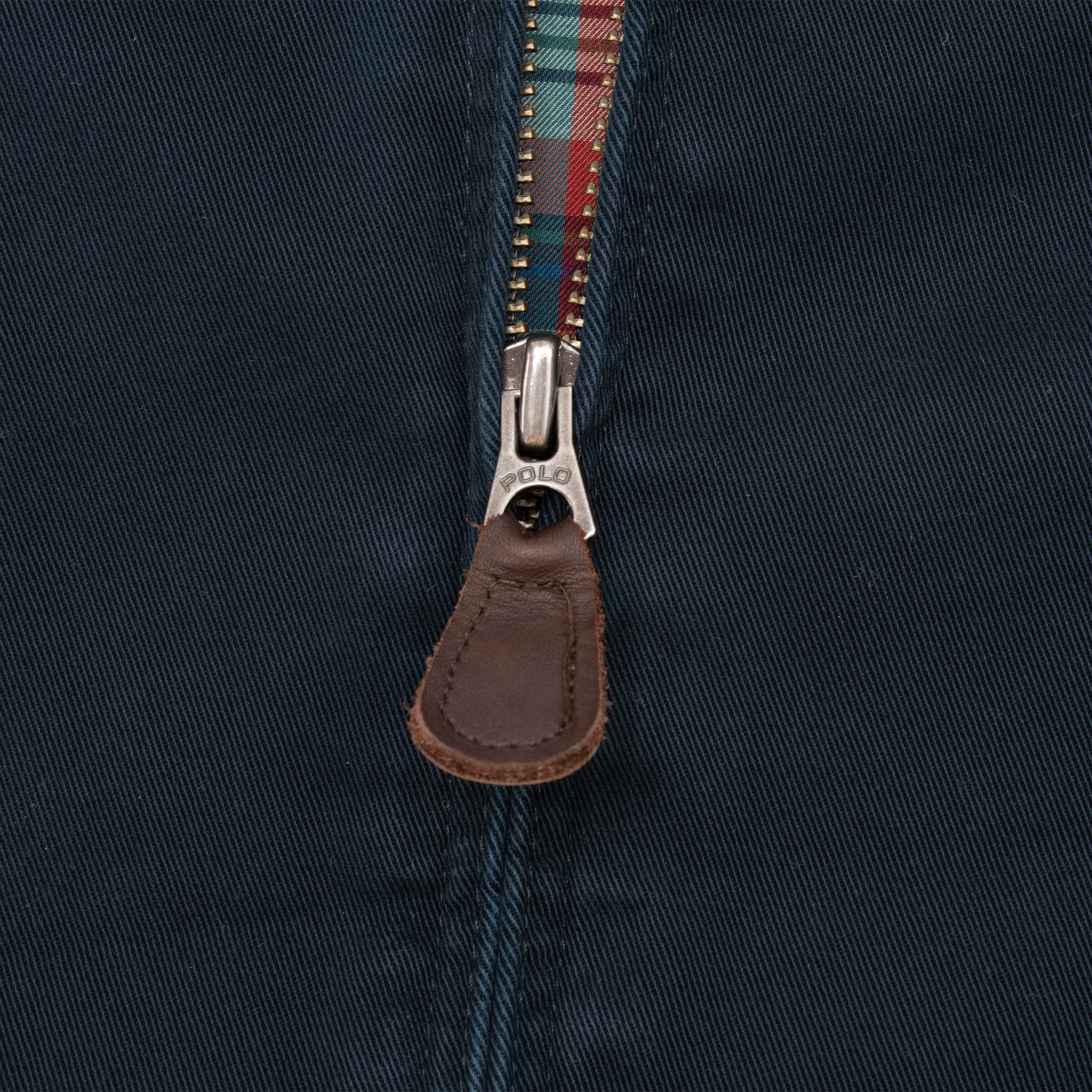 Close-up of metal zipper and brown leather pull on navy jacket