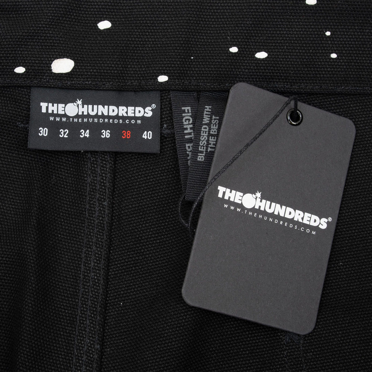 The Hundreds waistband label and hangtag on black paint-splatter jeans